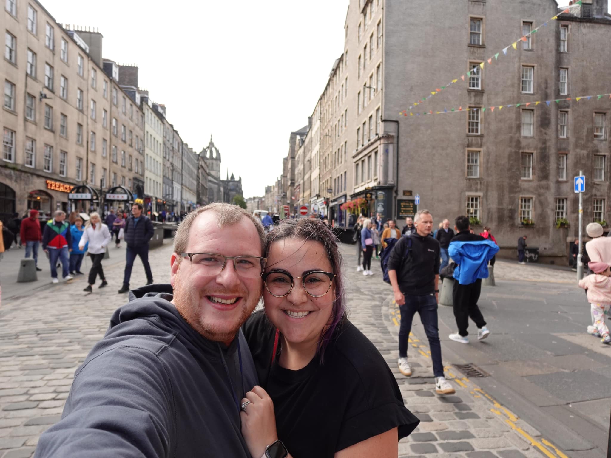 A couple posing for a selfie on a busy street with many people walking
