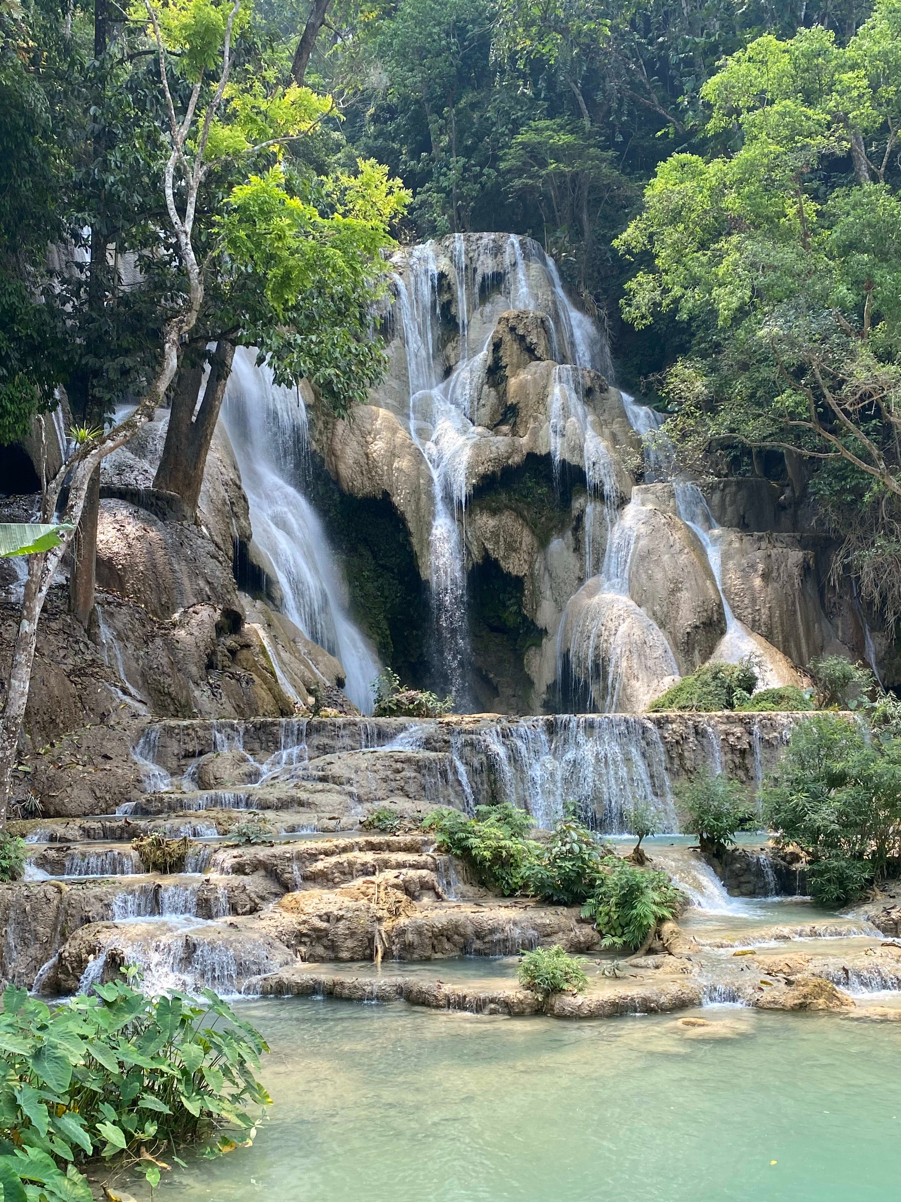 Picture of Kuang Si Waterfall, a multi-tiered waterfall with lush forest all around it.