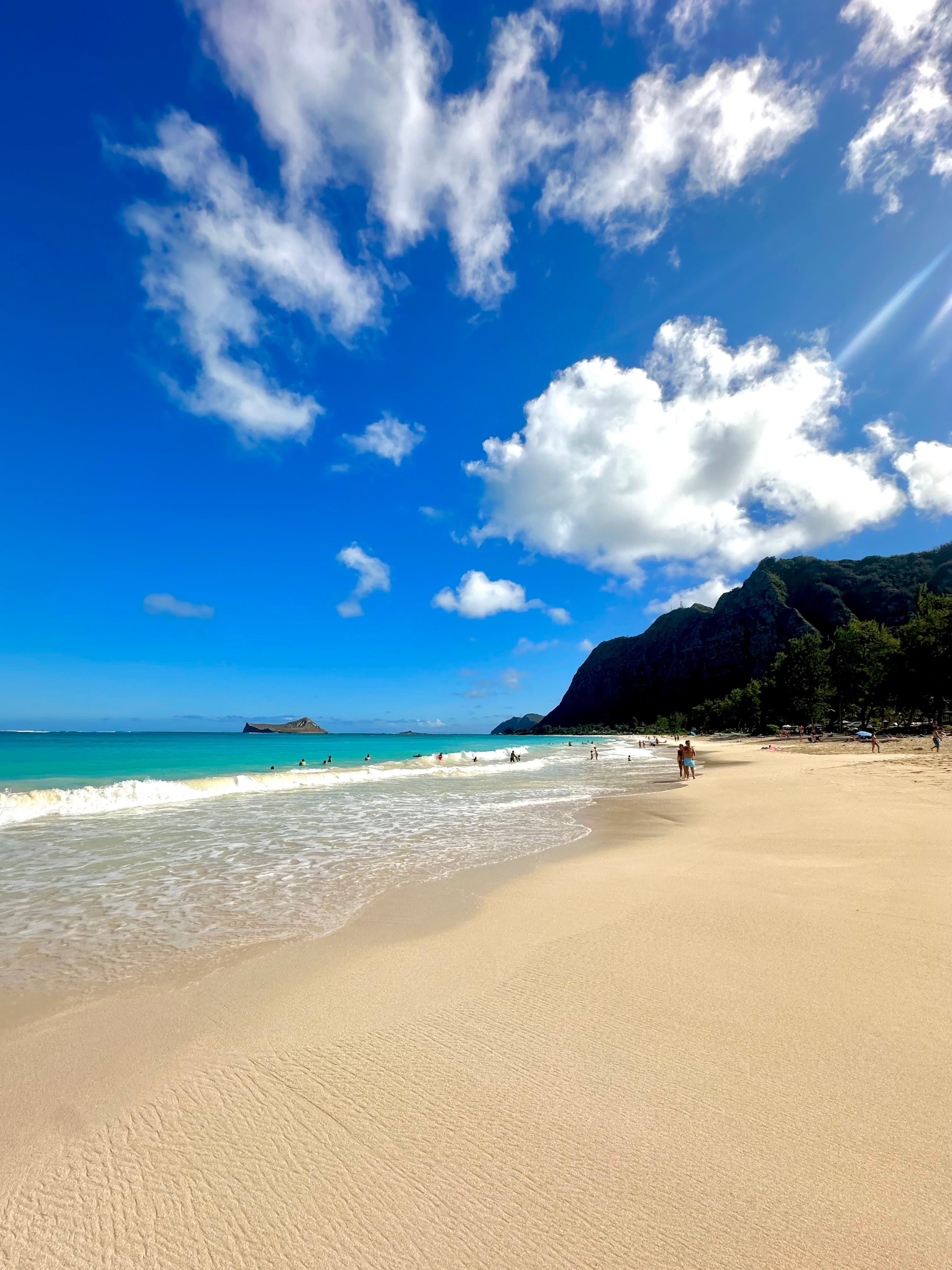 A golden beach with turquoise water on a bright blue day with scattered white puffy clouds