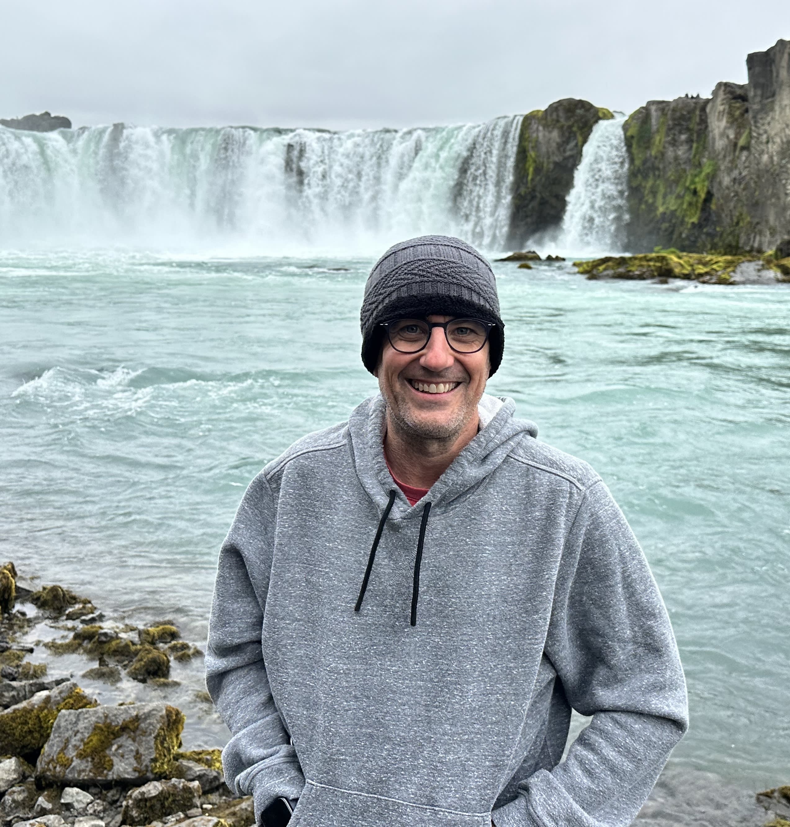 Picture of Dave in a hoodie and beanie in front of a waterfall