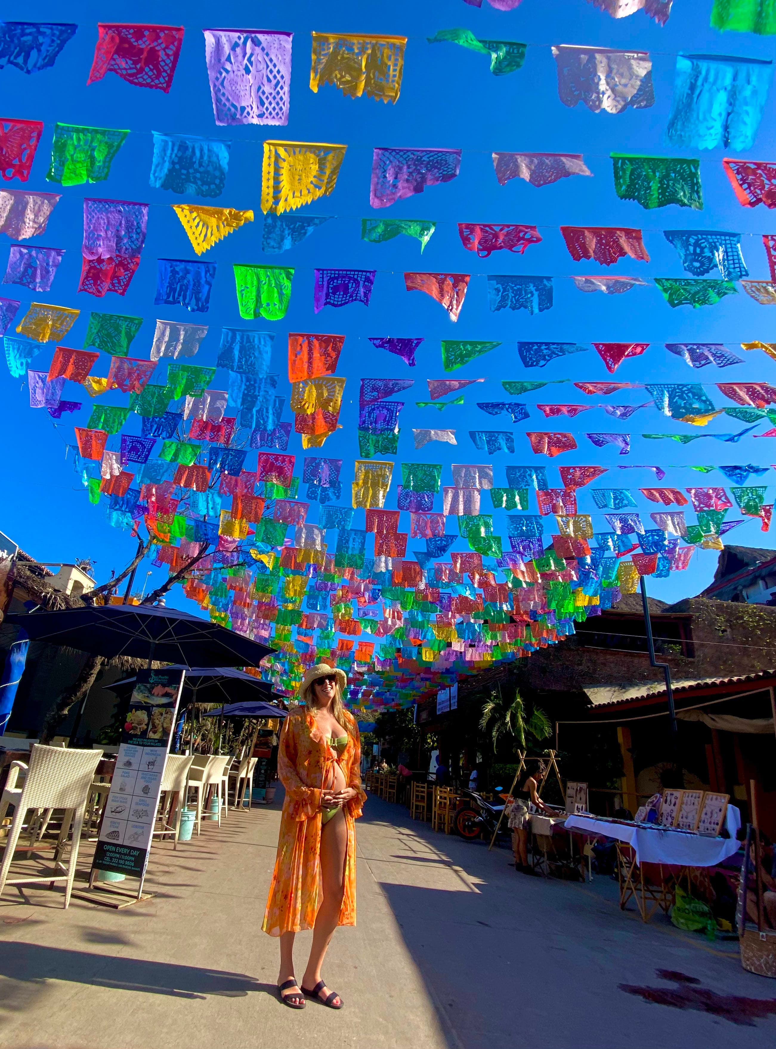 Chelsea posing on a street with multi-colored flags hanging overheard