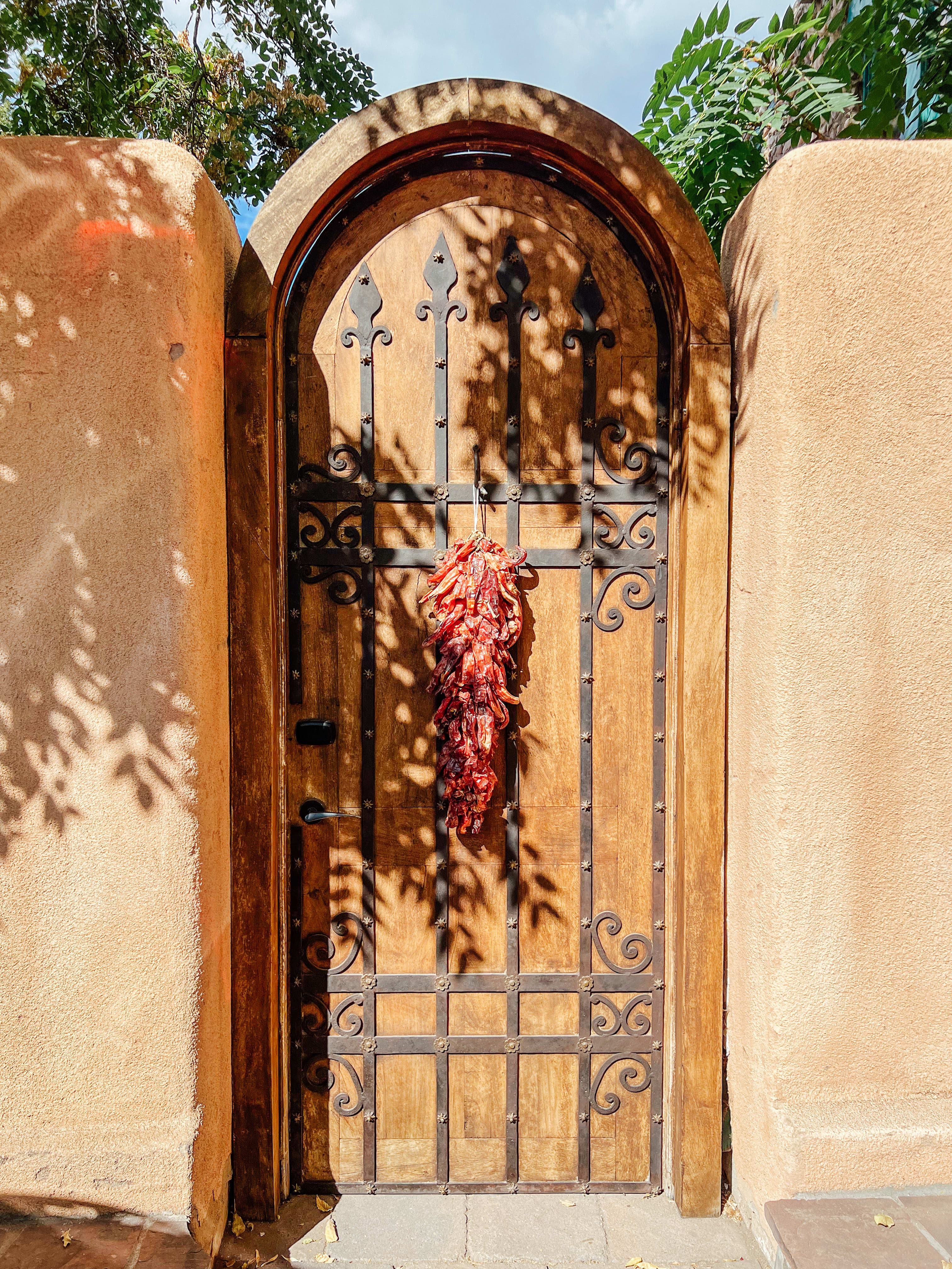 A wooden and wrought-iron door with a bunch of chilis hanging from it.