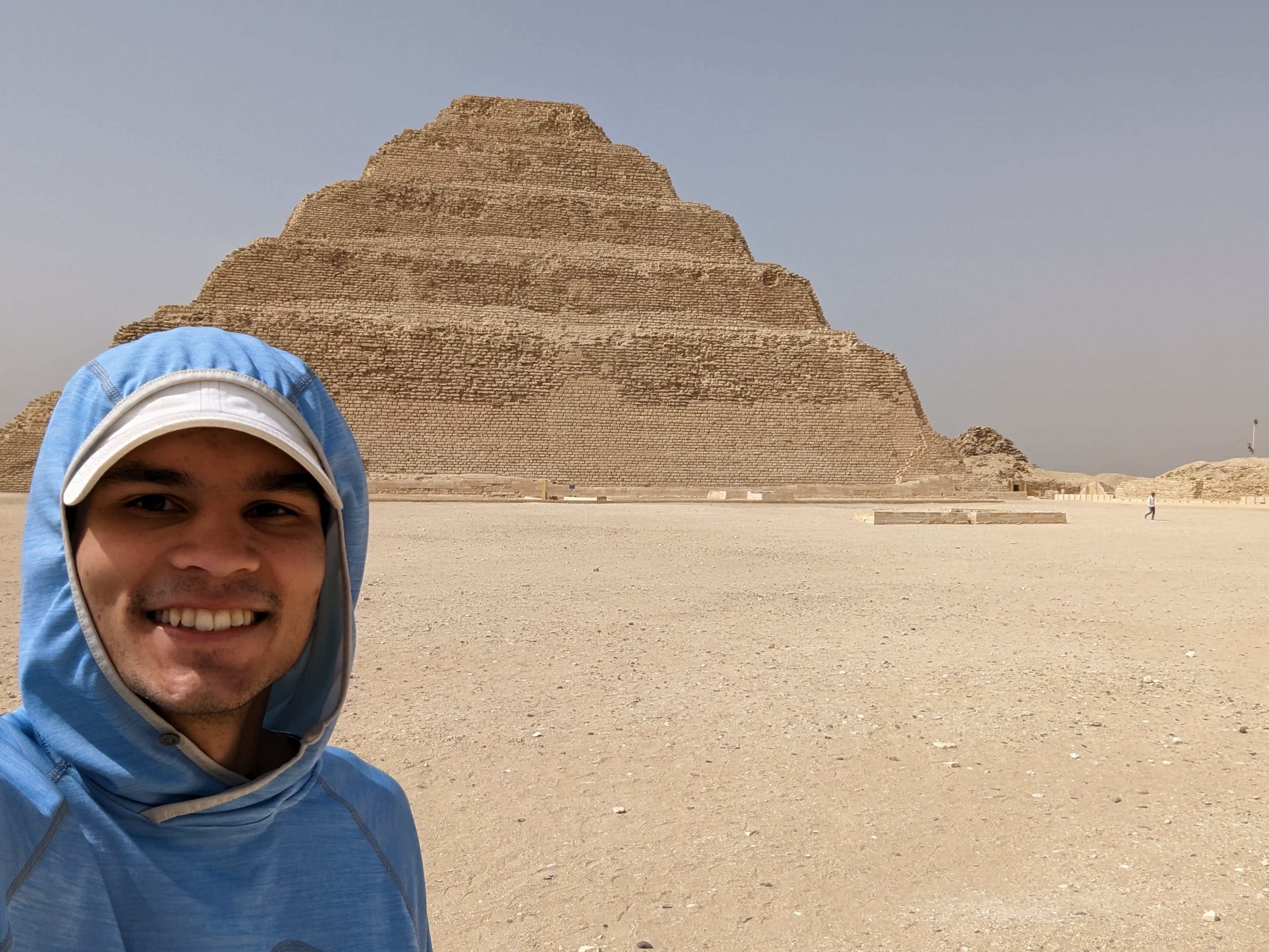 Jackson in a blue jacket taking a selfie with a step pyramid in the desert.