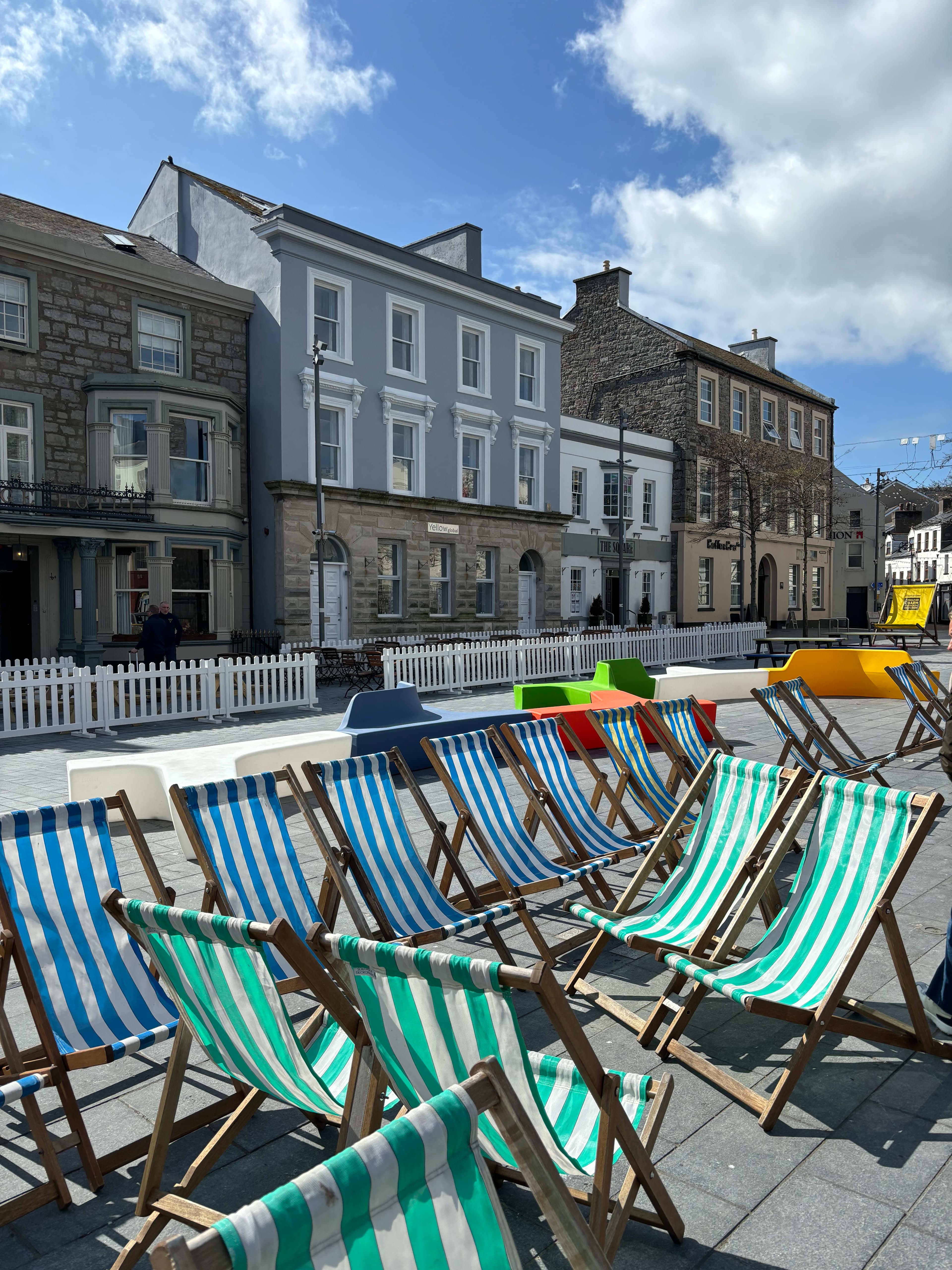 Blue, green, and white striped chairs on the side of a street with small buildings in the background