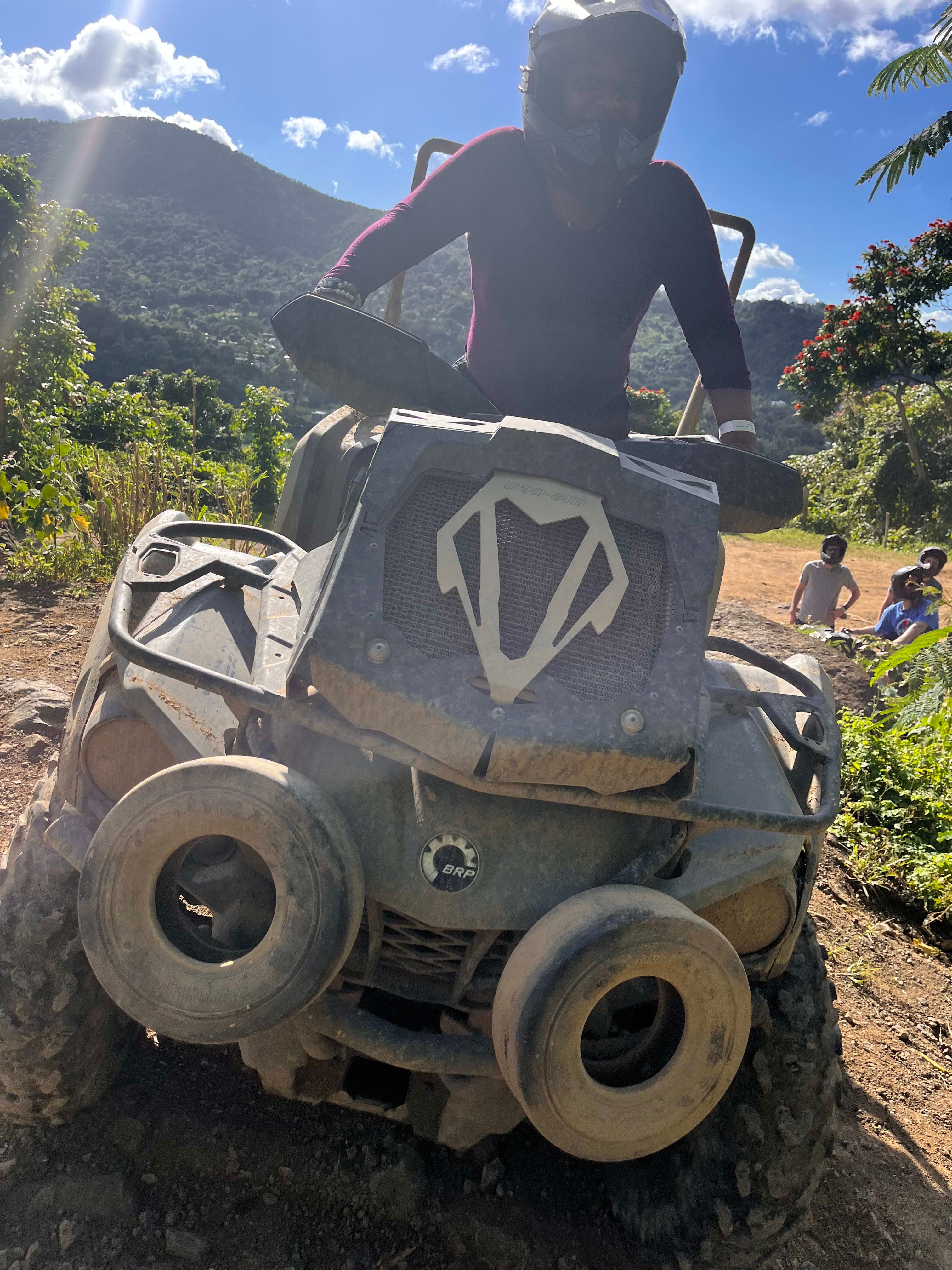 Ashley wearing a helmet on a dusty ATV in the mountains on a sunny day
