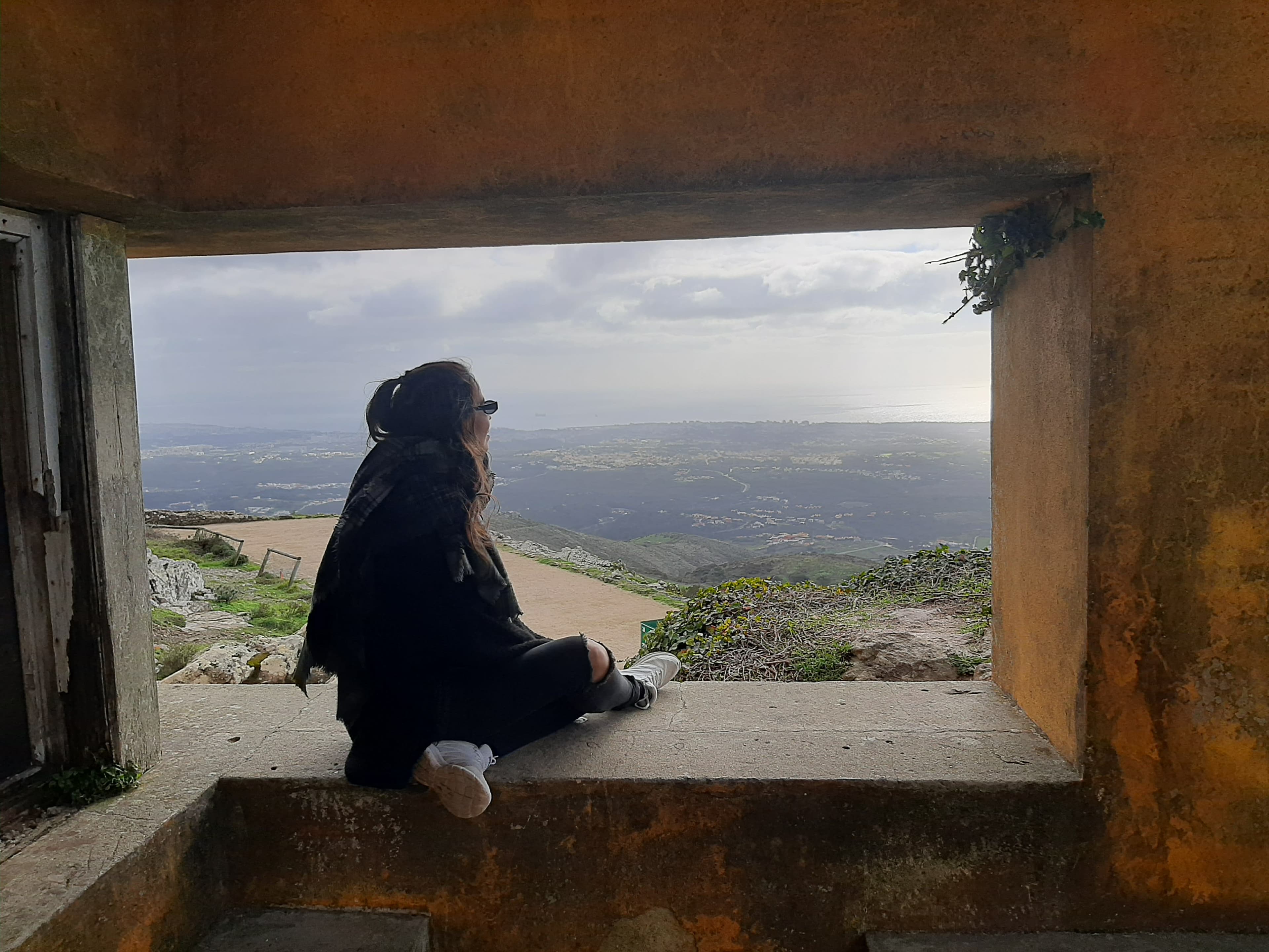 Picture of Mariana sitting in a window with beautiful view of a green landscape on a cloudy day