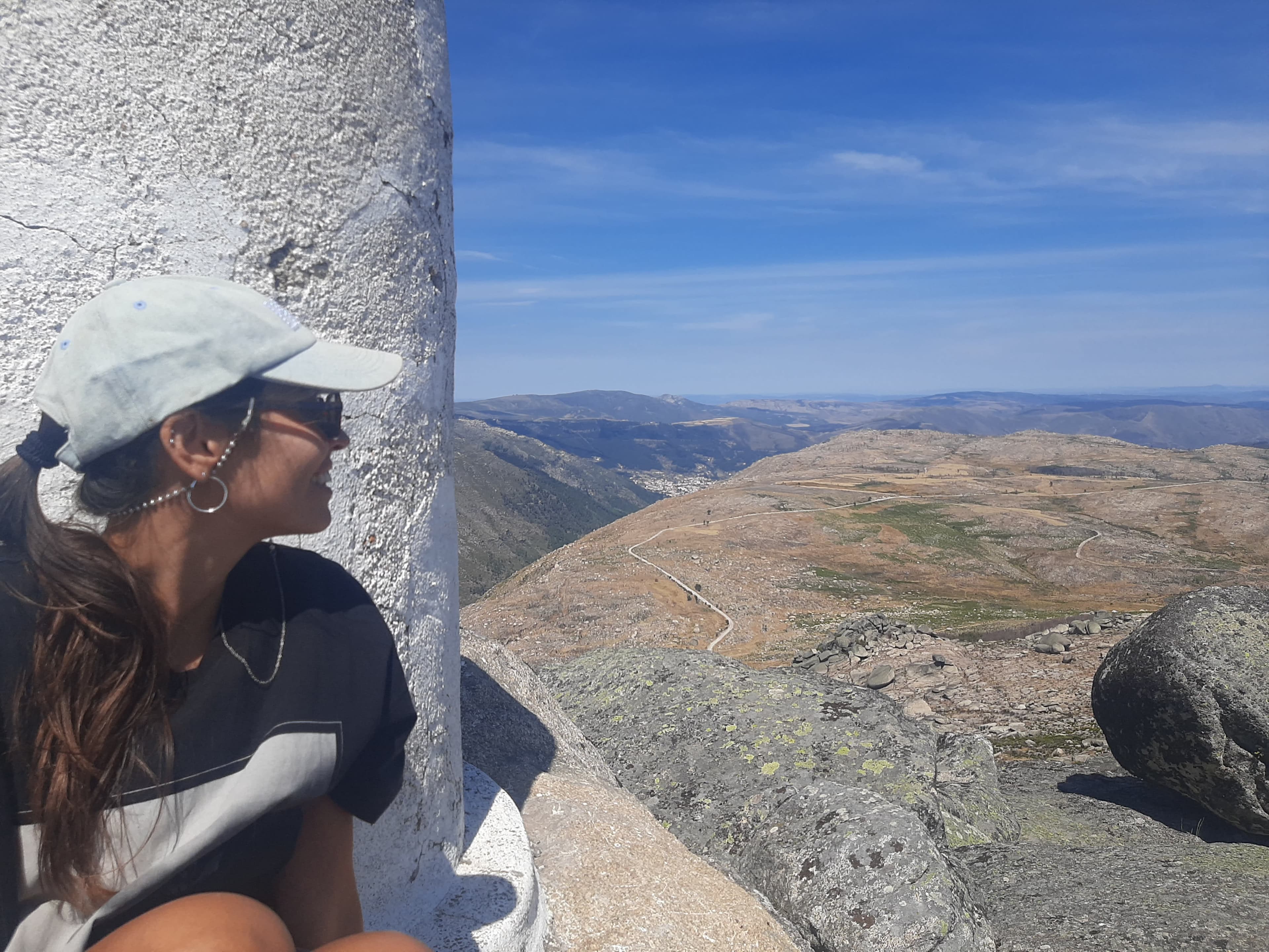 Picture of Mariana wearing a white baseball cap looking out to a beautiful mountain landscape on a clear day