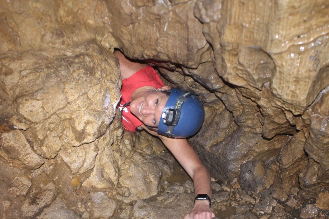 Picture of Dayna in a blue helmet smiling as she rock climbs at Cavernas de Venado