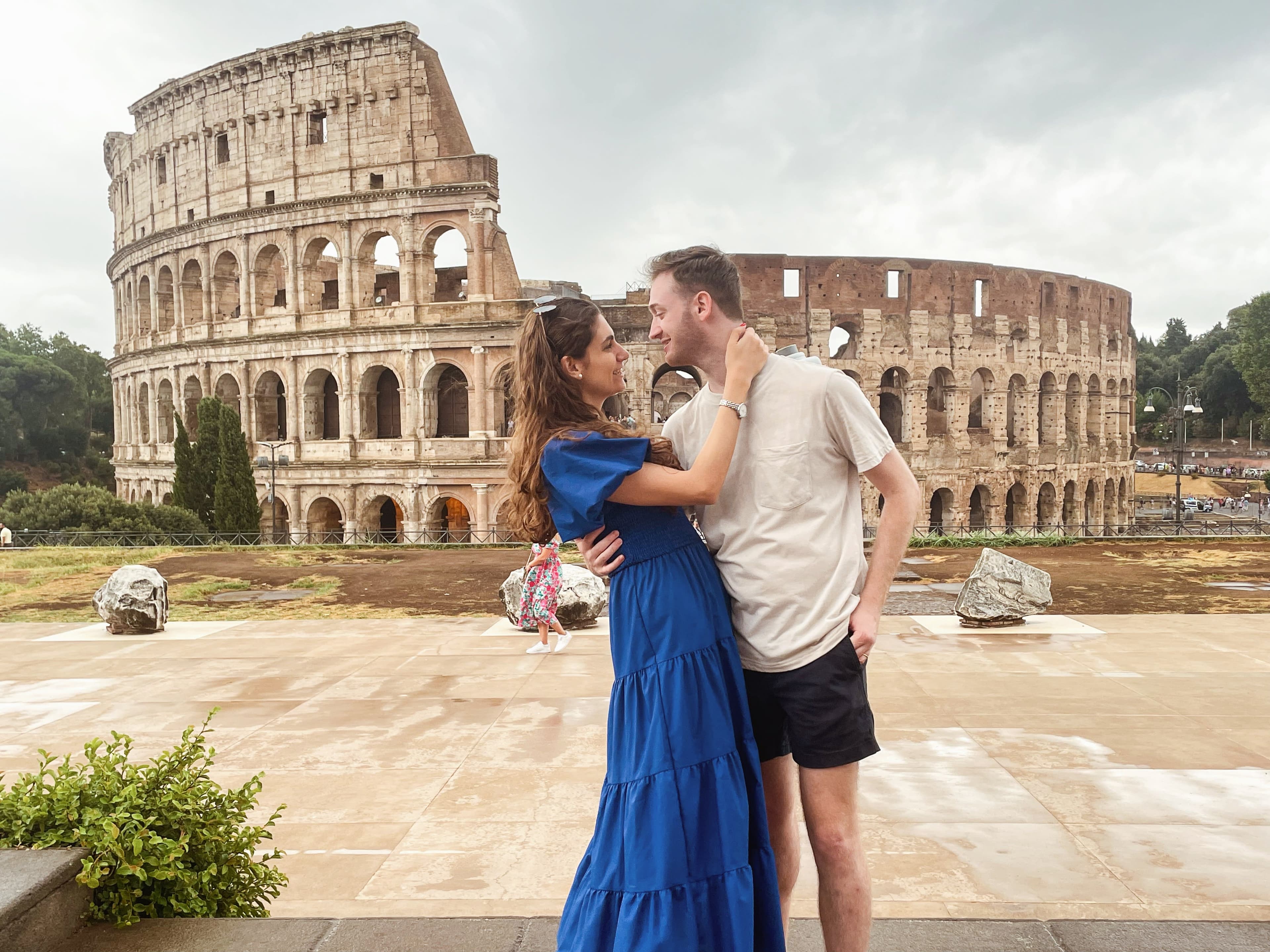 Ashley in a blue dress posing in a romantic pose with partner in front of the Colosseum