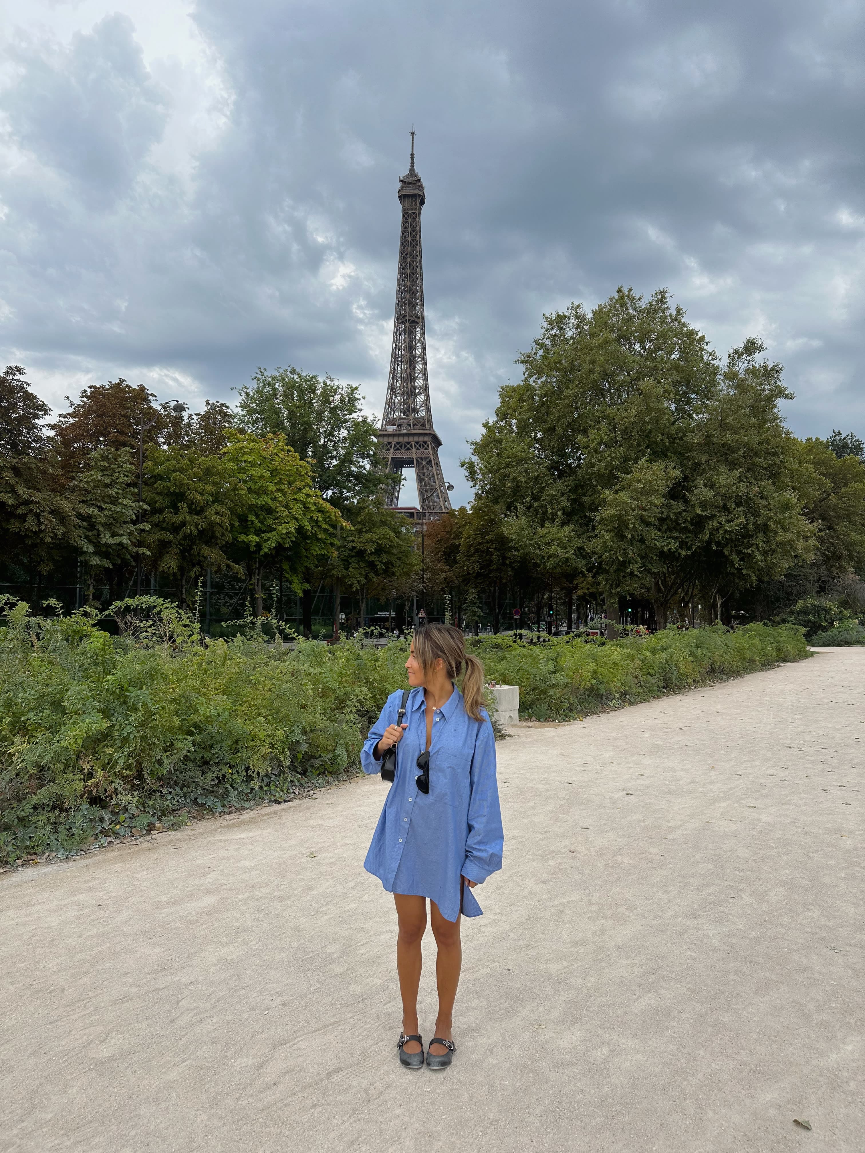 Jamie in a blue dress posing for a photo with the Eiffel Tower in view in the background