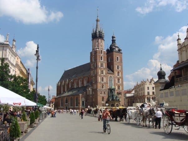 View of the St. Mary's Basilica Church in Kraków, Poland on a busy street with people on bicycles and horse drawn carriages parked in a line