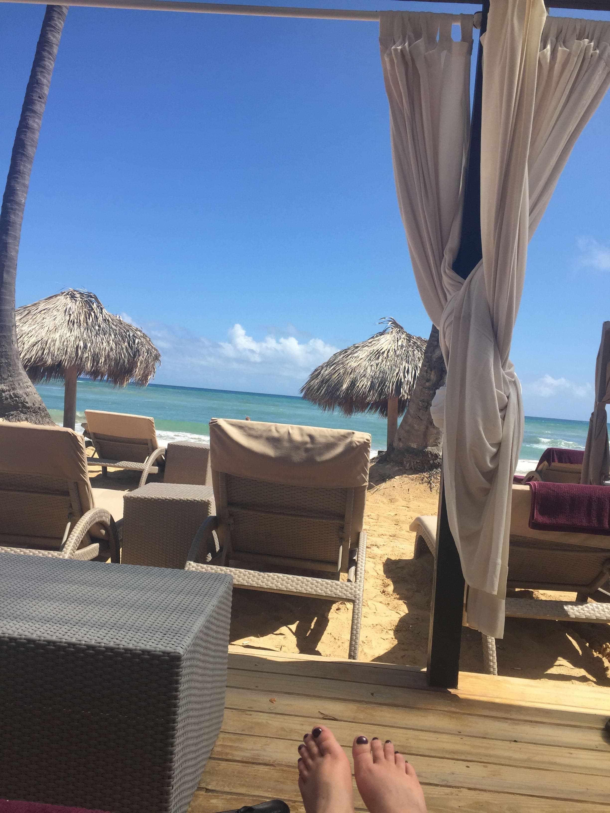 A photo taken from a lounge chair looking out to other lounge chairs and straw umbrellas on the beach.