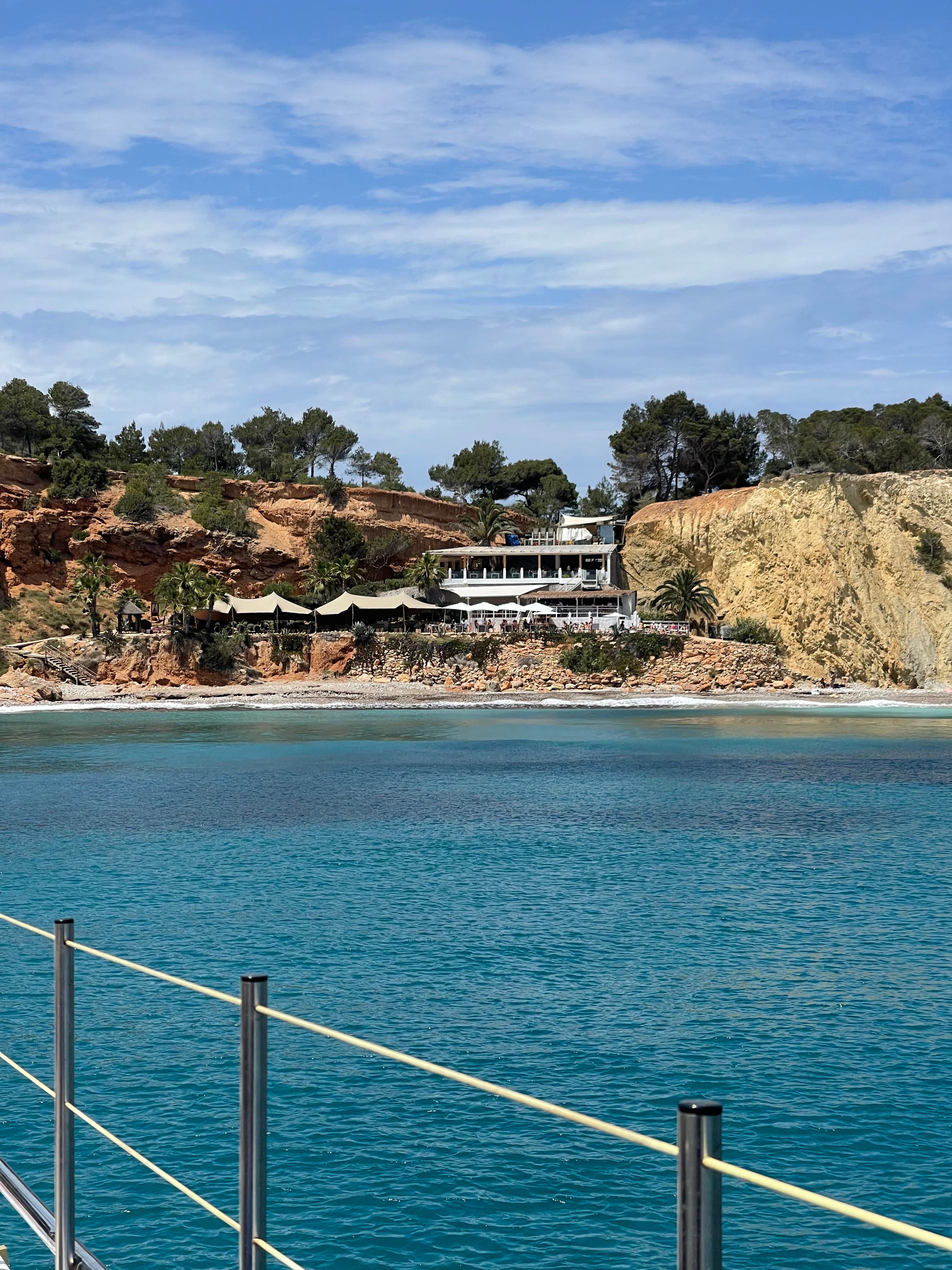 Picture of a beautiful cliffside home and small beach below from a boat deck above the sea