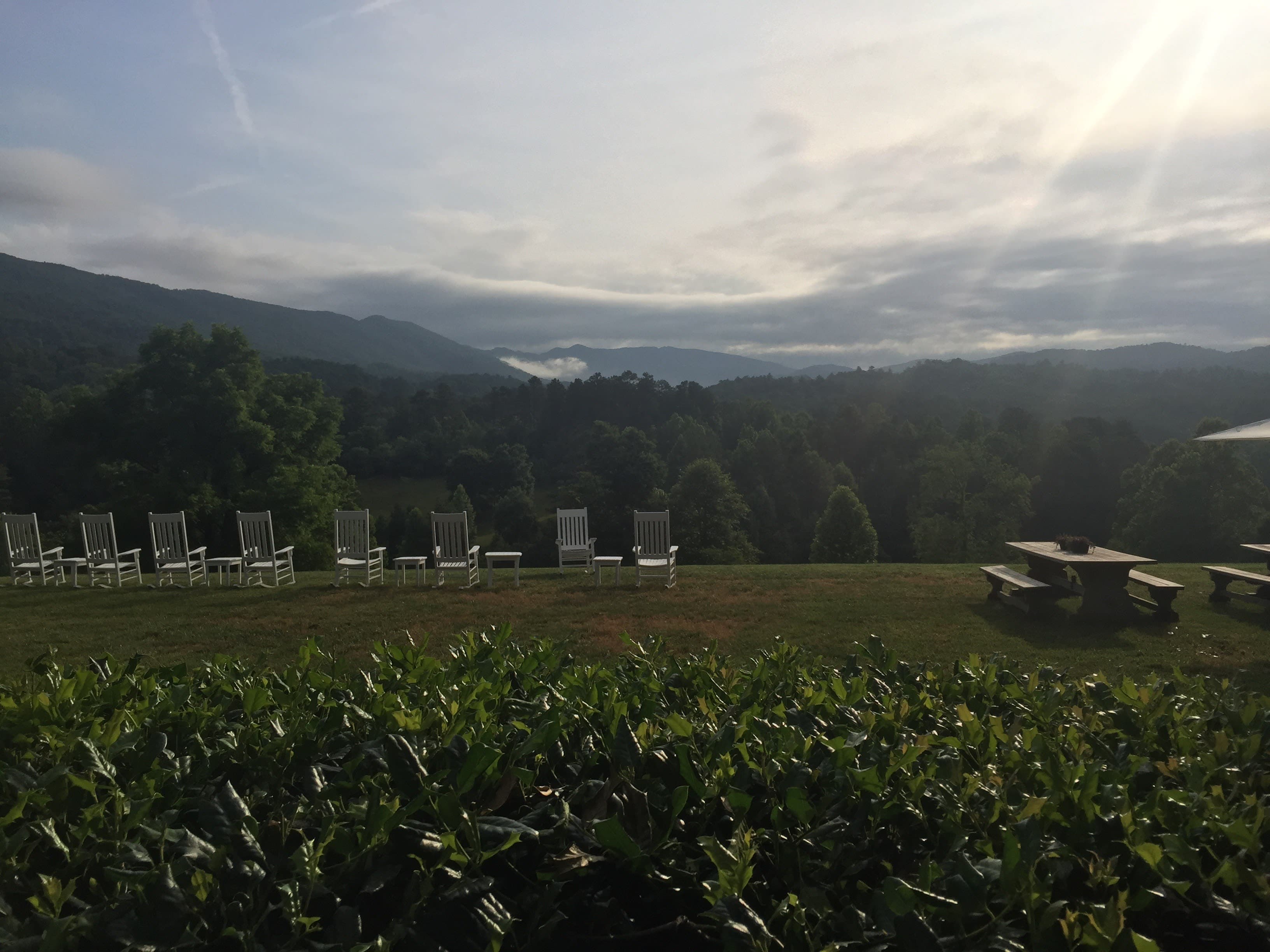 a green field with lawn chairs and the sun shining over mountains on the horizon