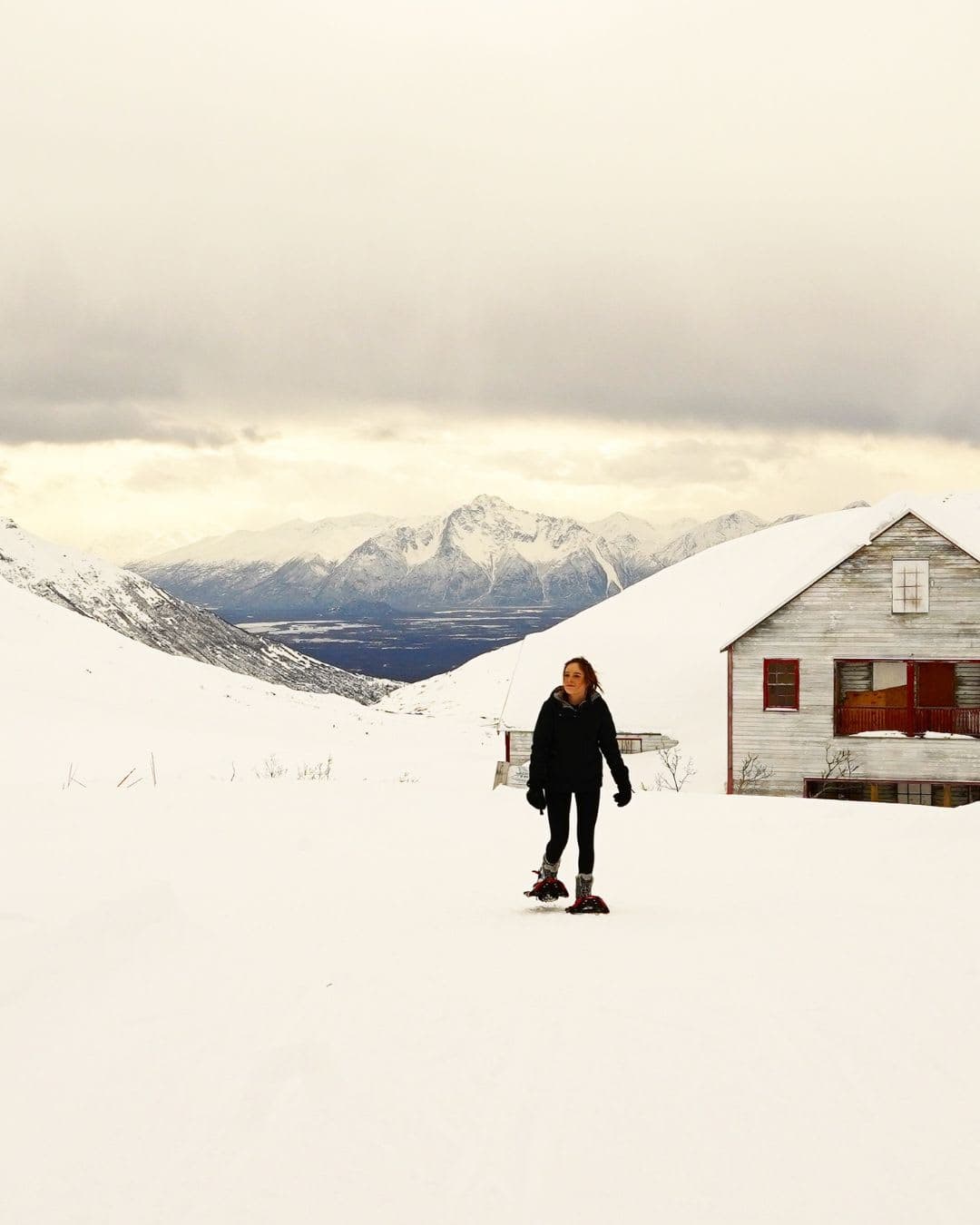 Advisor in winter clothing walking through snowy hills with a small white house behind her