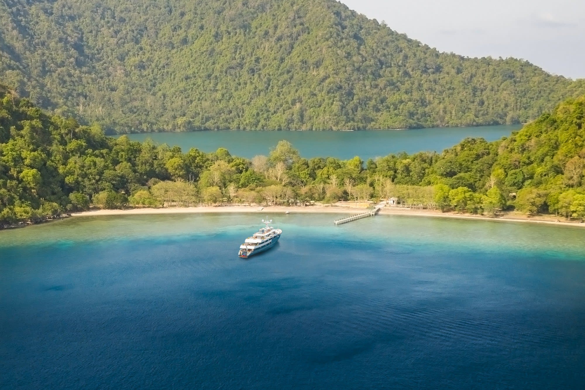 a white yacht prepares to dock at a pier in a lush island lagoon