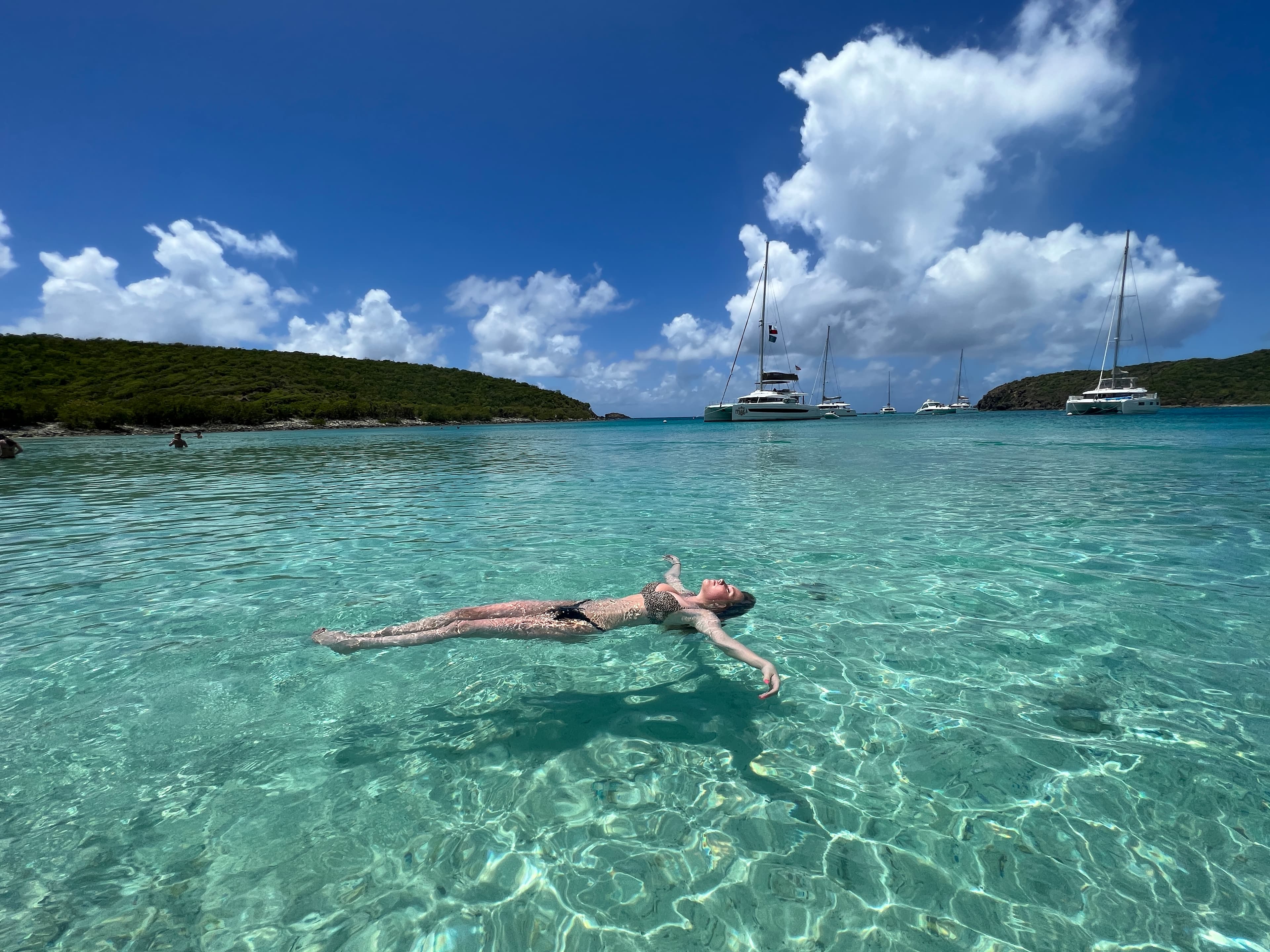 Advisor floating in the crystal clear ocean on a sunny day with boats in the distance.