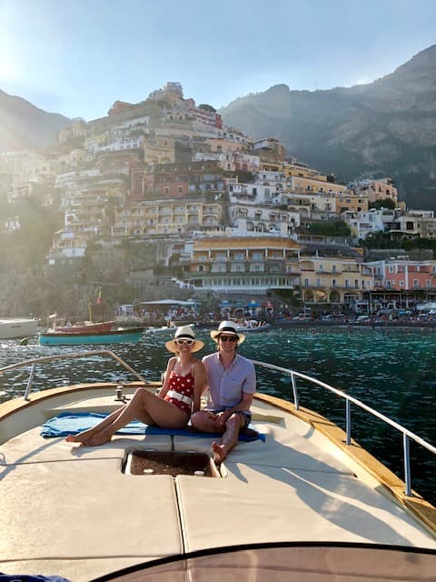 Advisor and partner on the front of a boat at sea with the Amalfi coast behind them