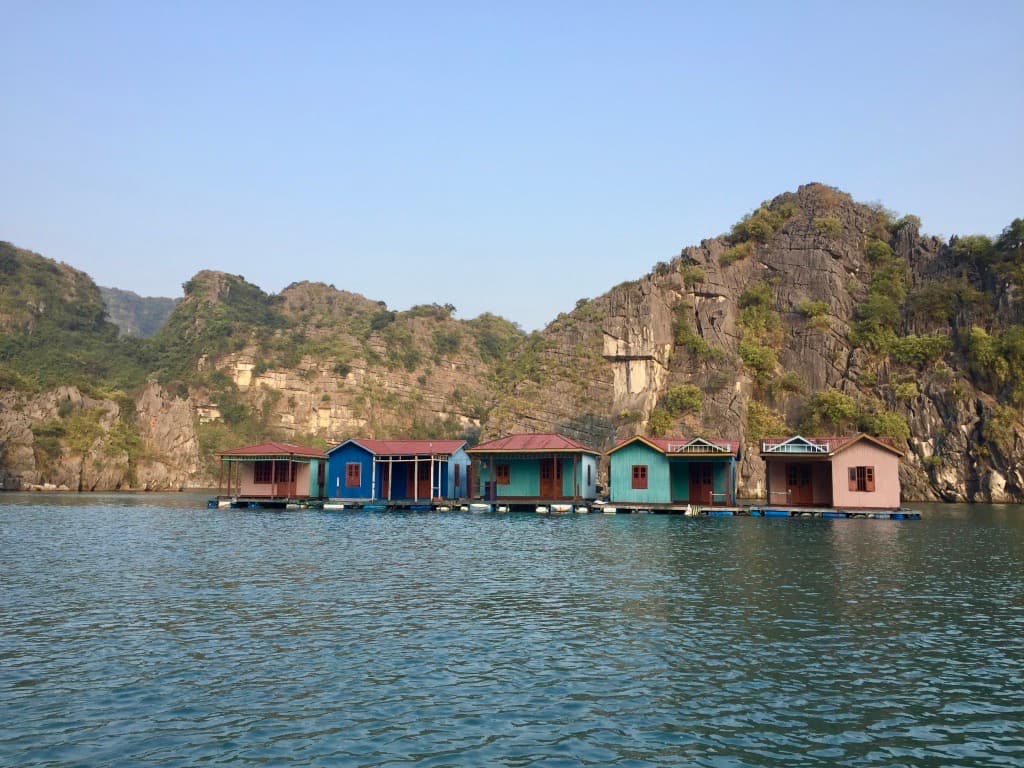 An image of colorful houses across a body of water with mountains in the distance on a sunny day.