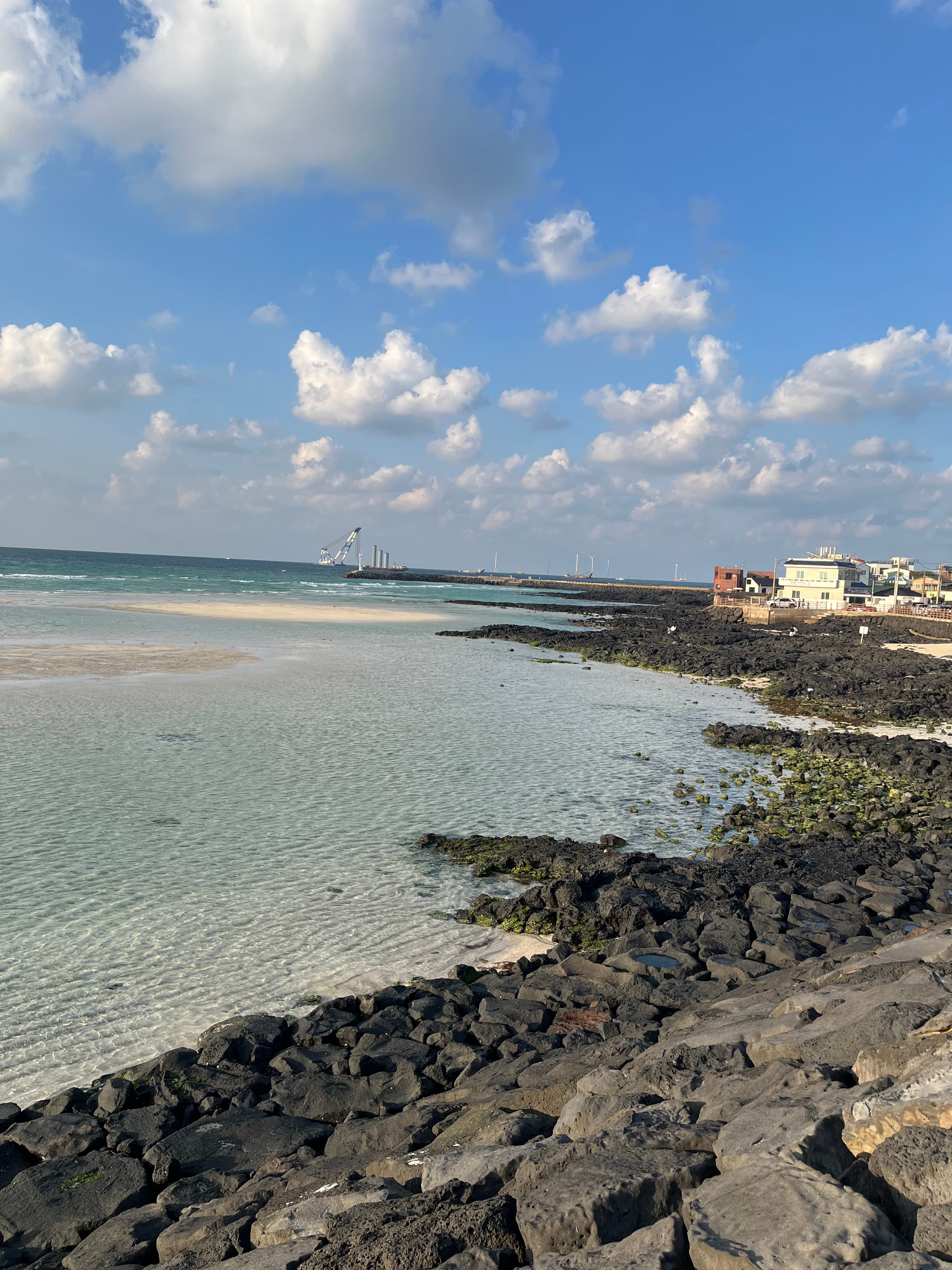 A view of a rocky shoreline with calm water in the distance on a sunny day.