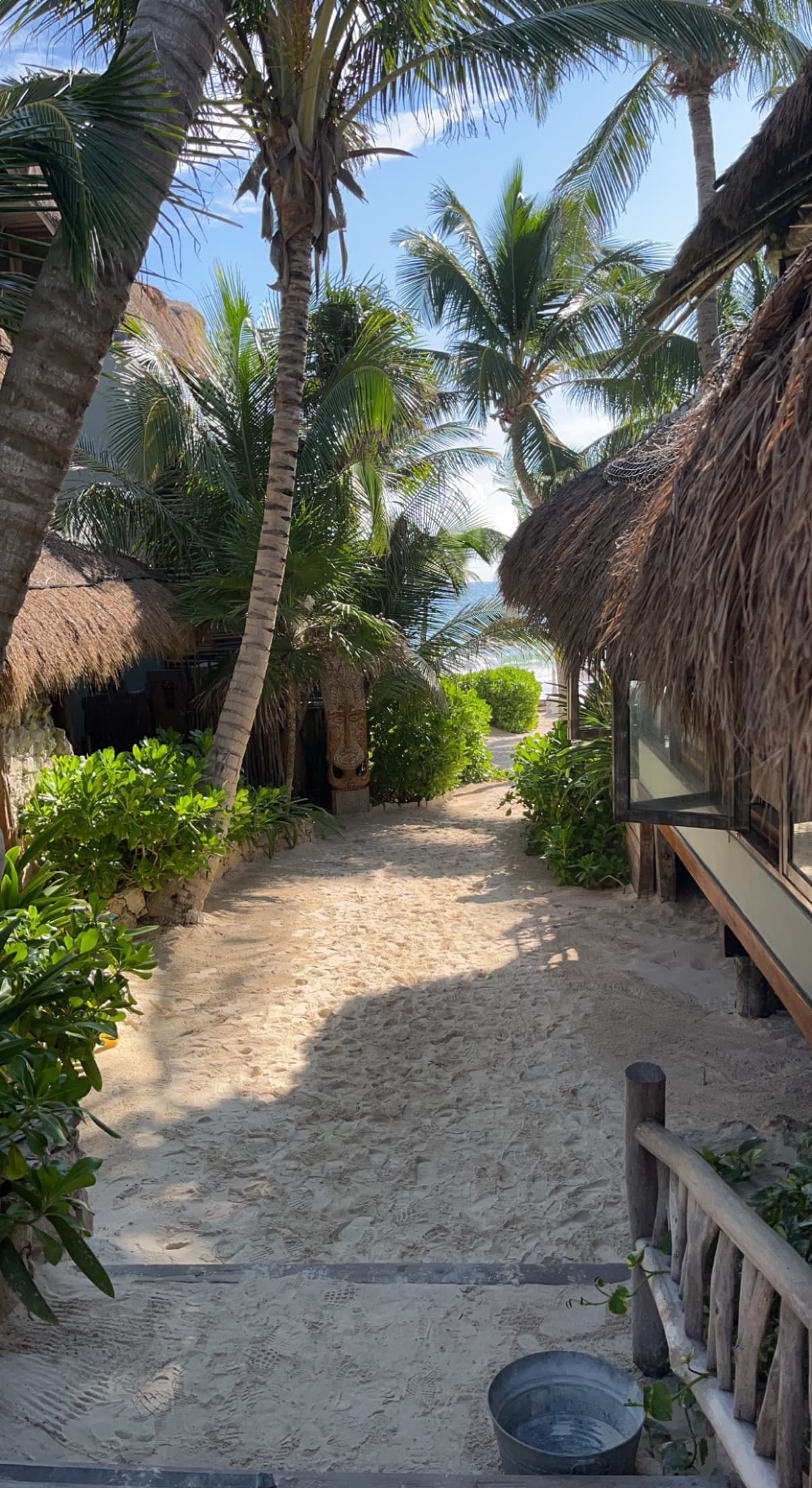 A view of sandy beach in front of palapa-style buildings leading down to the beach.