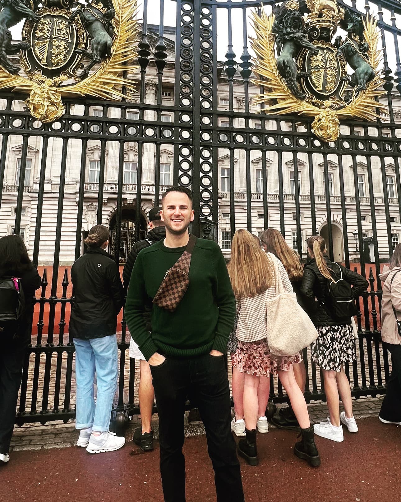 Travel advisor Taylor standing in front of grand black iron gates with gold features and a crowd looking through