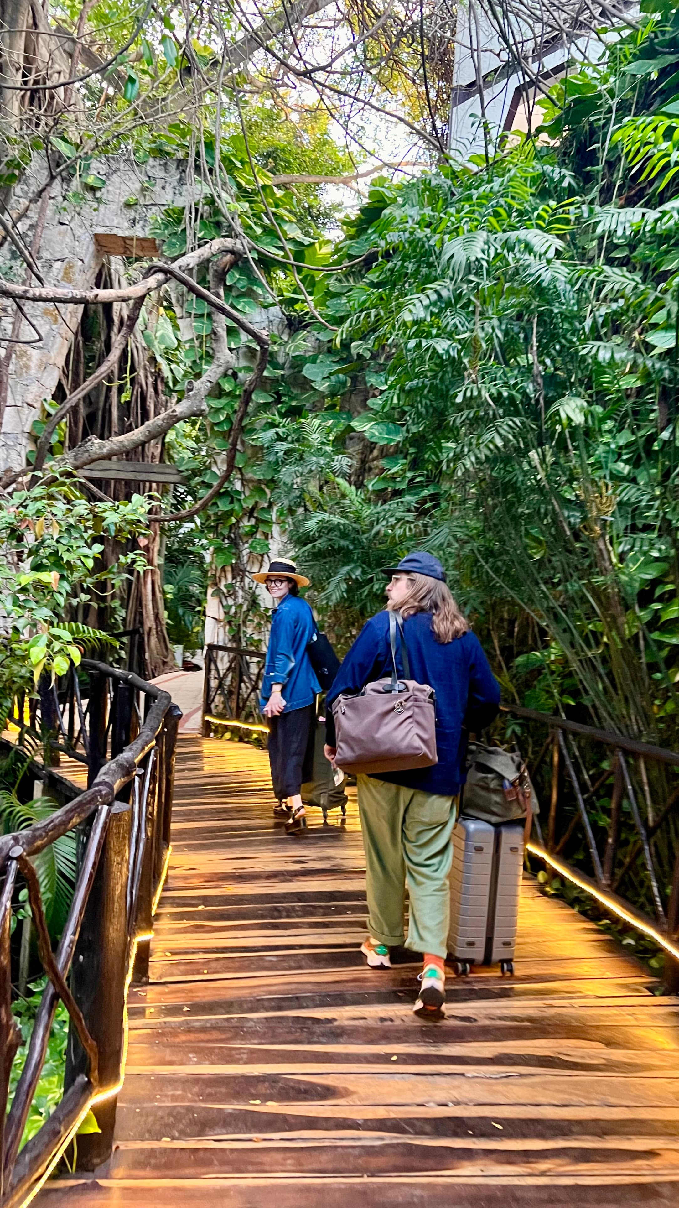Photo of two women with suitcases walking along a wooden bridge through trees