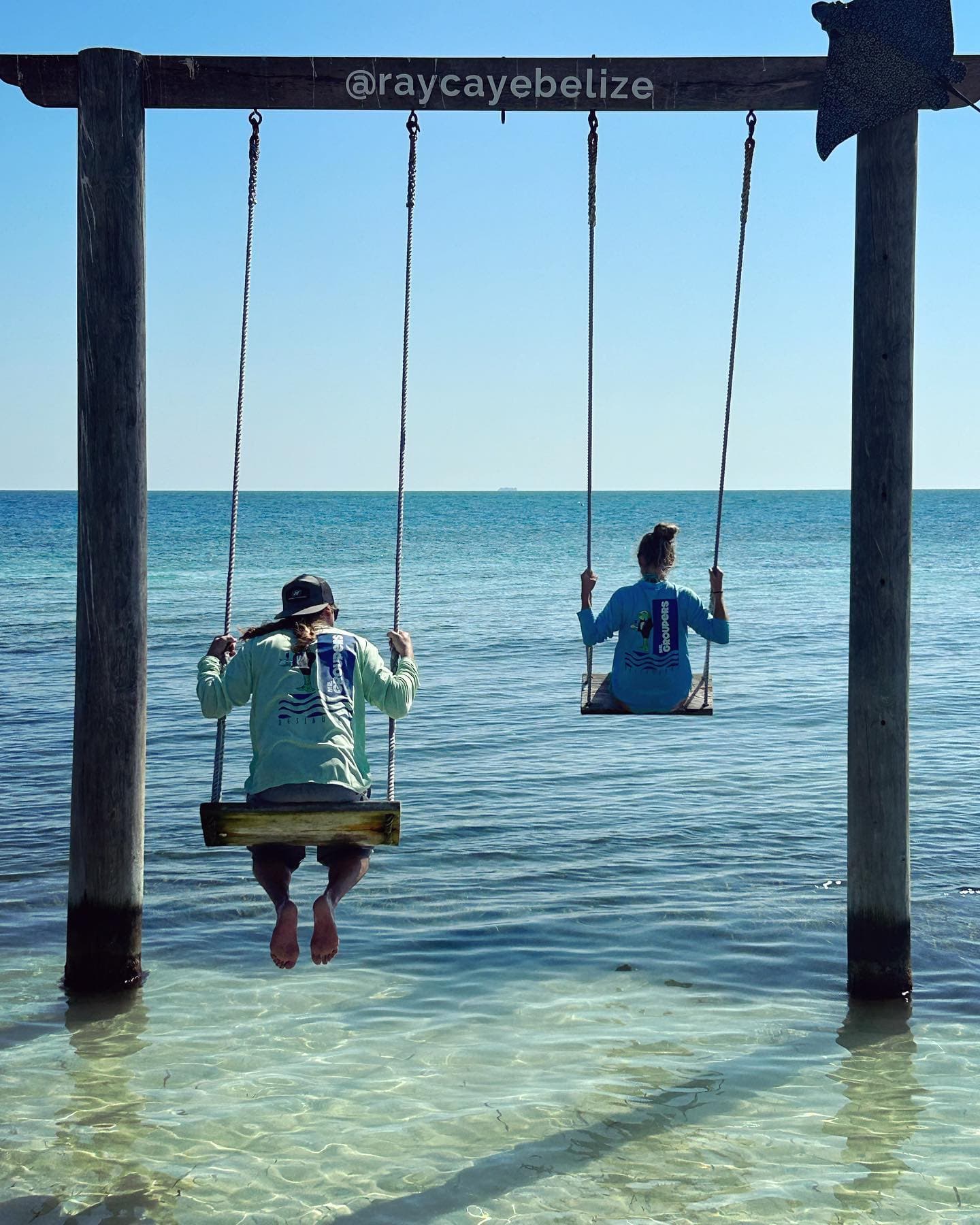 View of Maggie and another person on swings in shallow ocean water on a sunny day