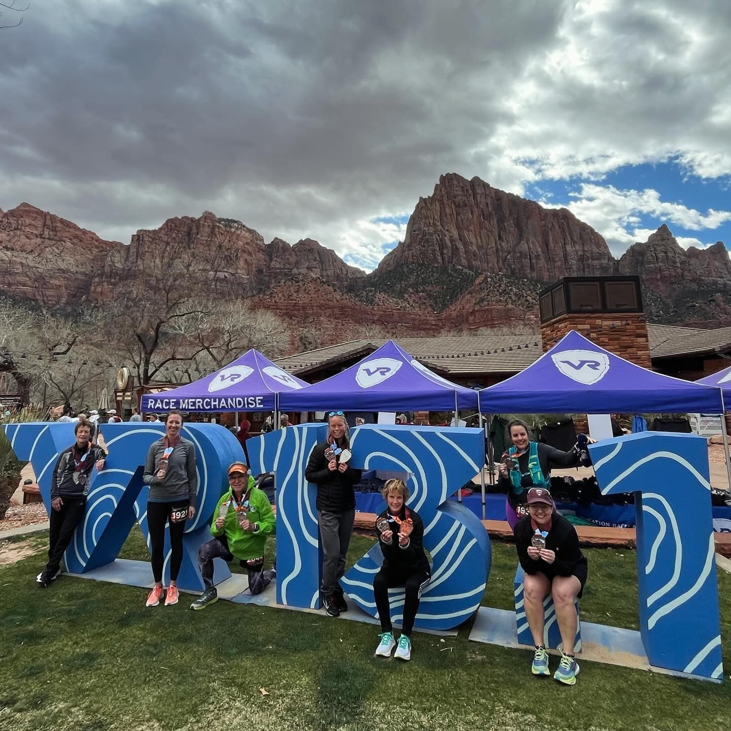 Image of Maggie and others posing in front of letters with a beautiful canyon background on a cloudy day