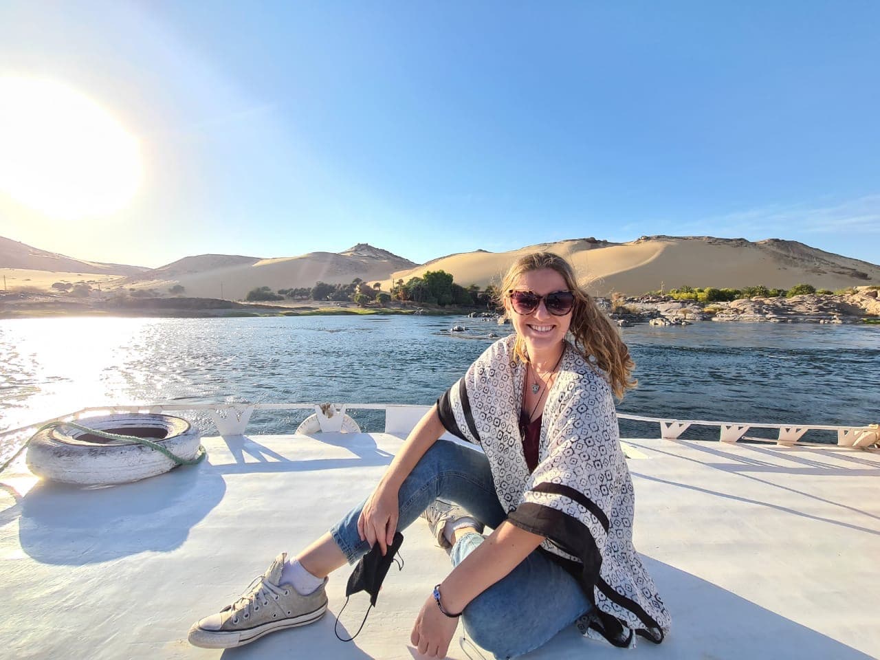 Kaitlin wearing sunglasses and sitting on the deck of a boat at sea with large sand dunes visible in the background