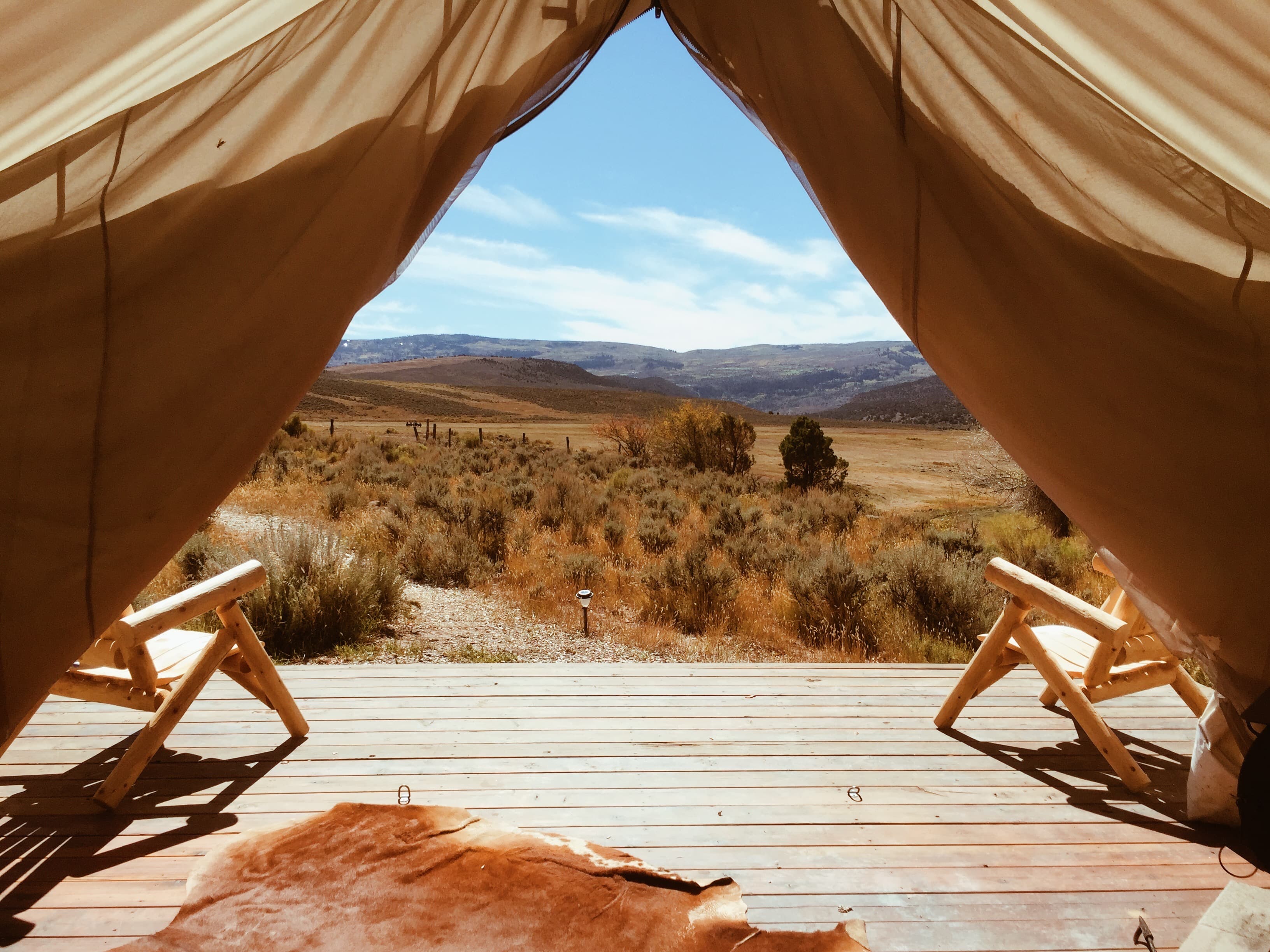 A view through a high end tent with chairs, a wooden deck and a desert setting in the distance on a sunny day.