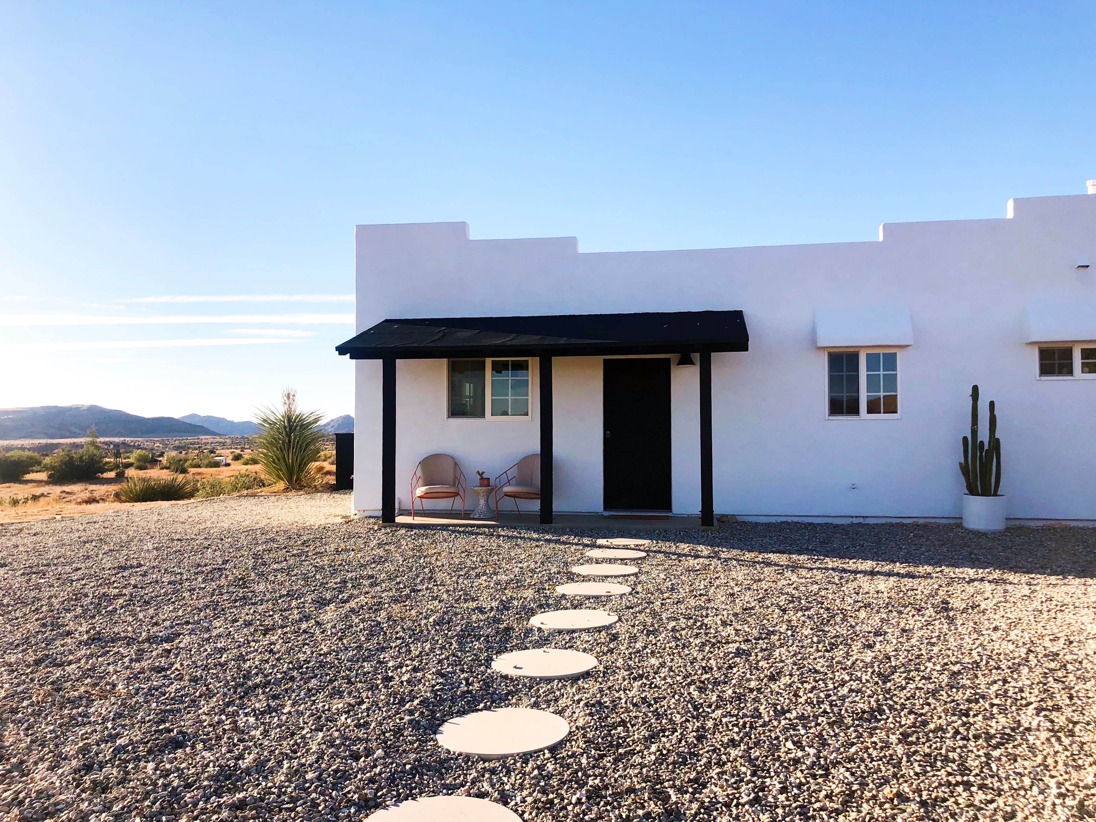A stone path leading to a white pueblo style house in the desert on a sunny day.