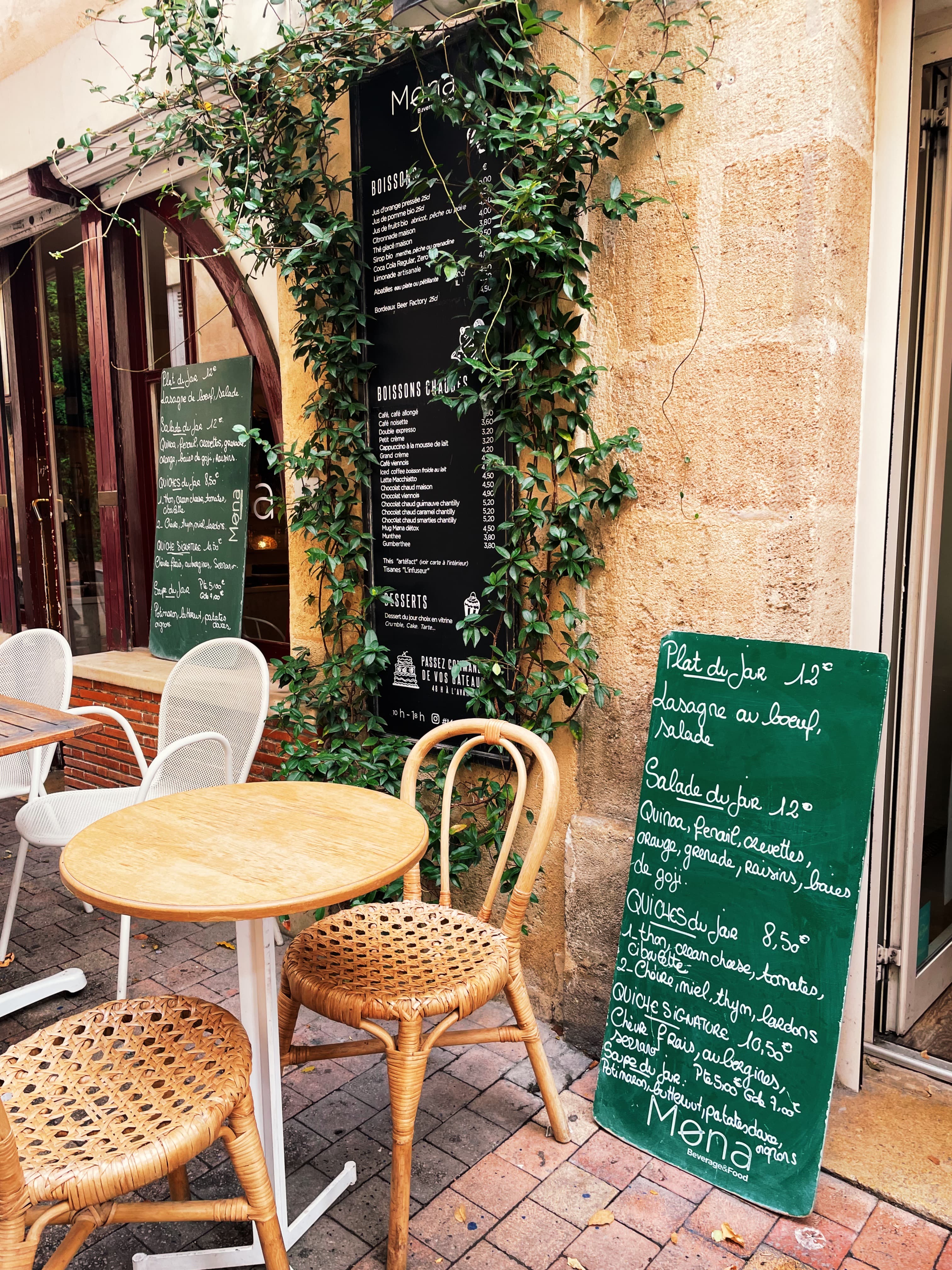 A view of an outdoor seating area at a restaurant with foliage on a sunny day.