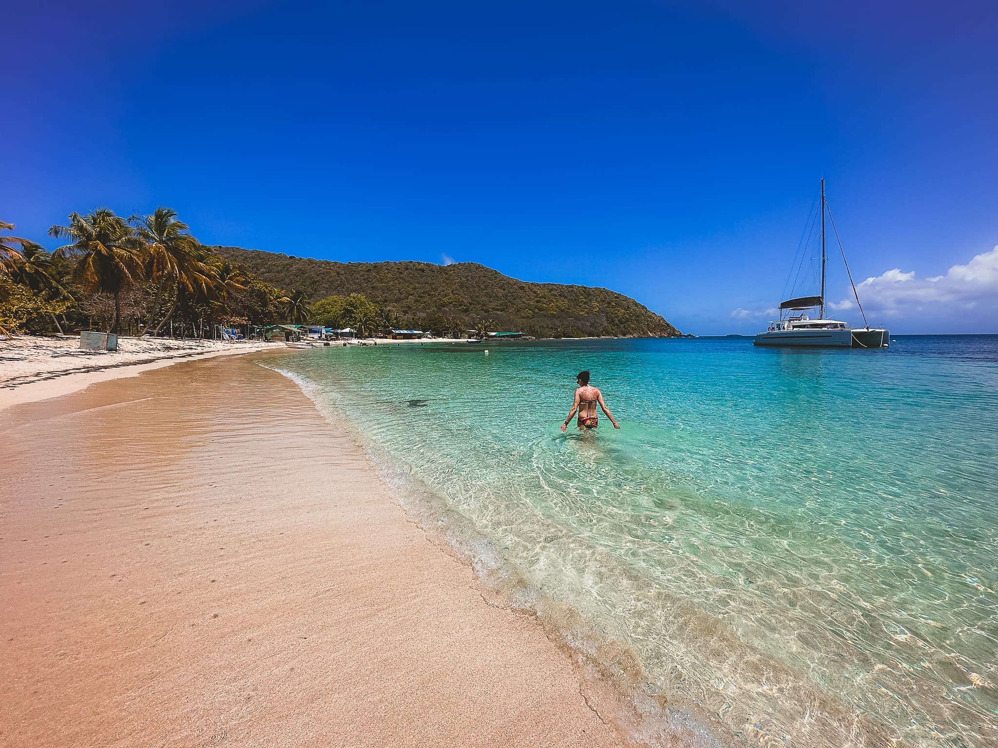 Advisor walking in the ocean on a sunny day with boats in the distance.
