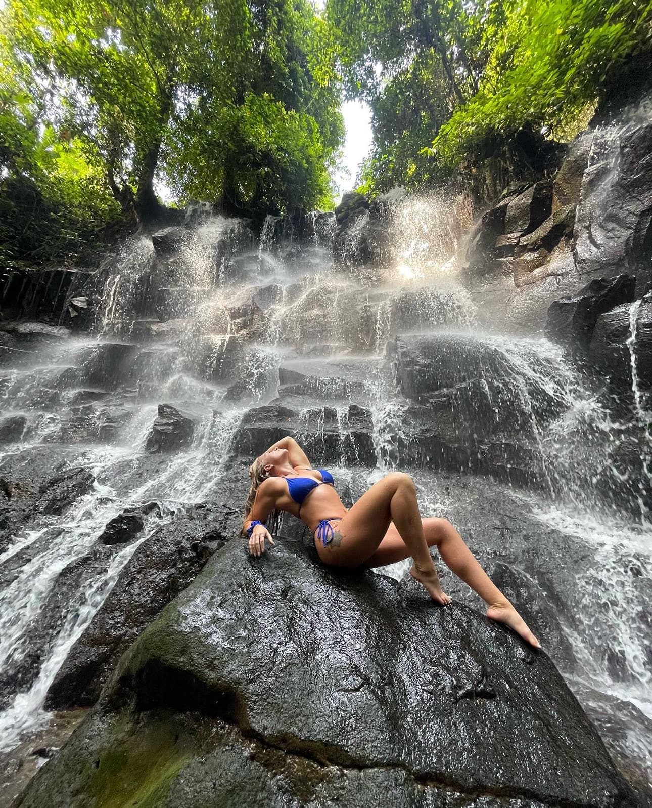 Advisor posing on rock at the bottom of a waterfall in a swimsuit.