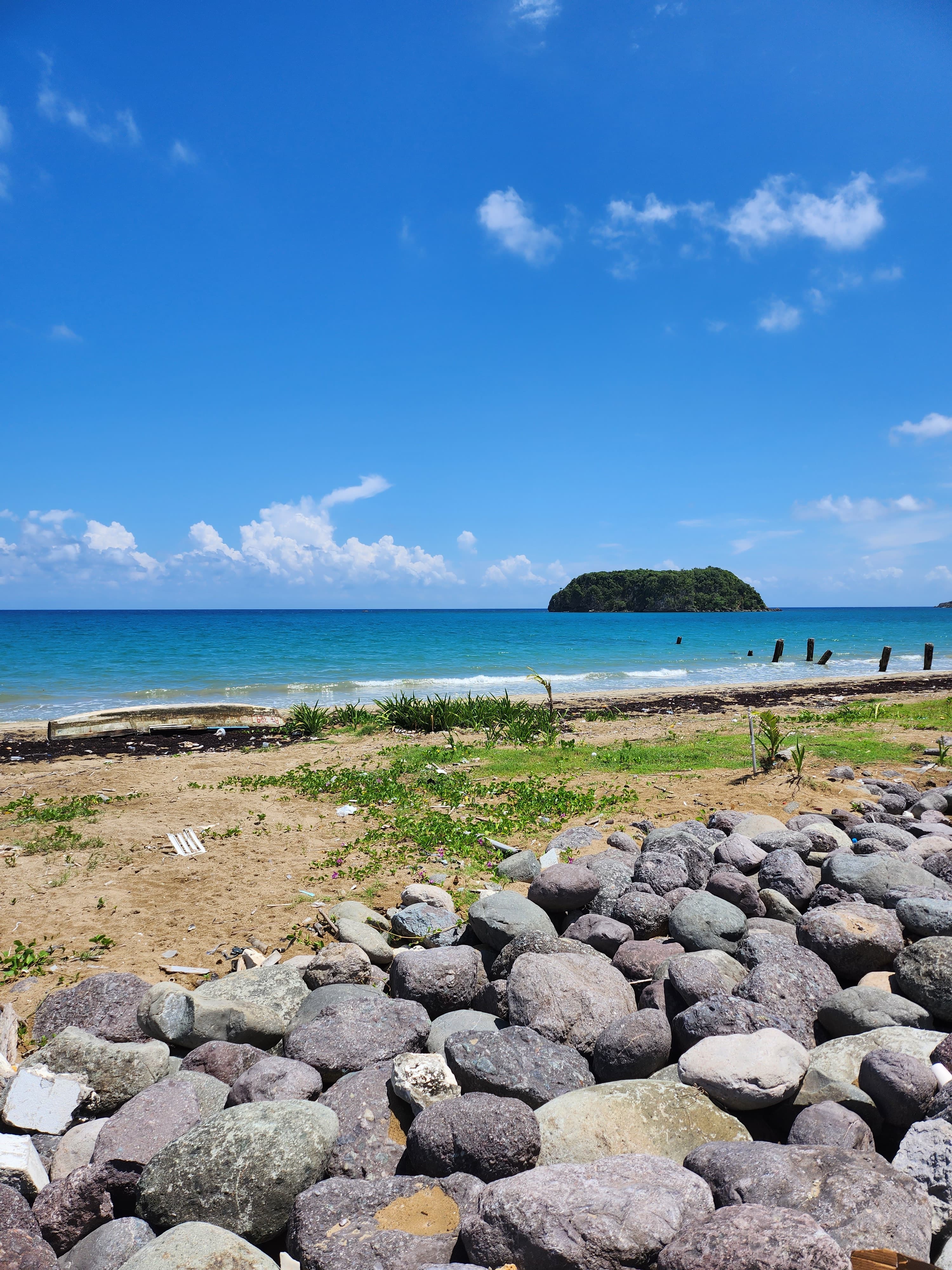 A view of the ocean with a sandy shore and rock formations in the distance on a sunny day.