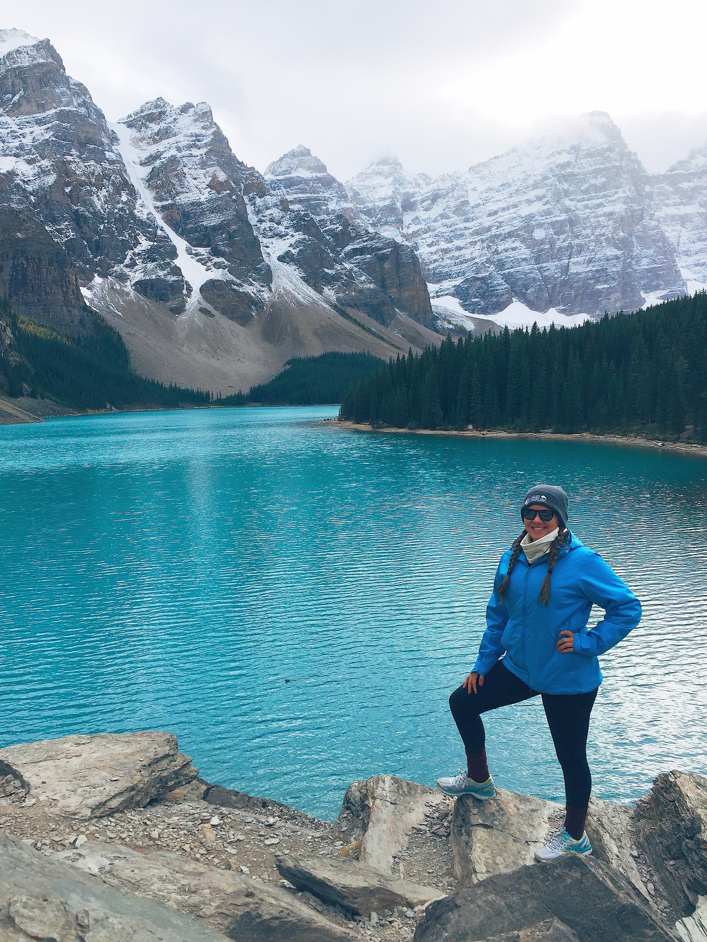 Advisor posing in front of a lake with mountains in the distance covered in snow.