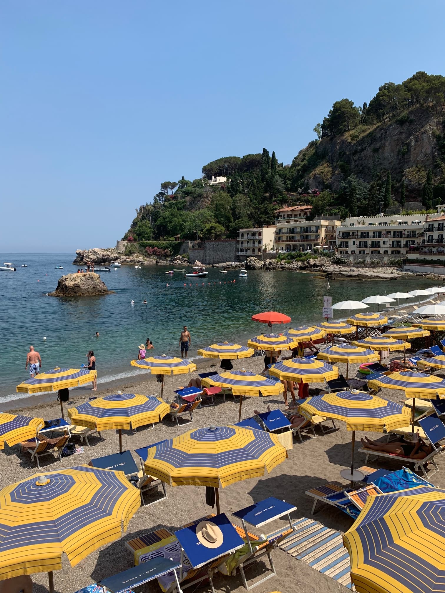 A beach view over looking blue and yellow umbrellas and calm water during the day.