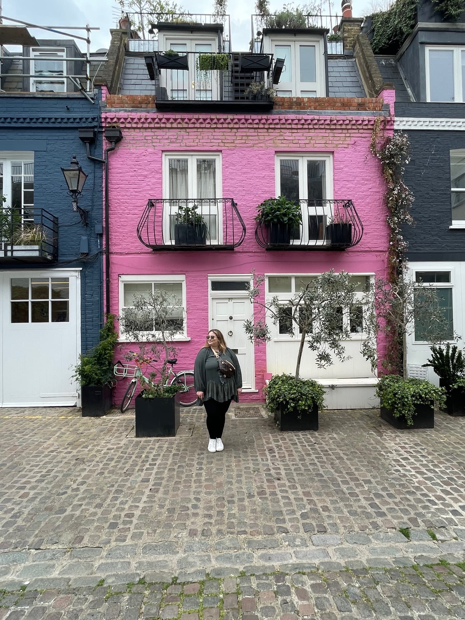 A person standing in front of a pink house with white trim and black balconies.