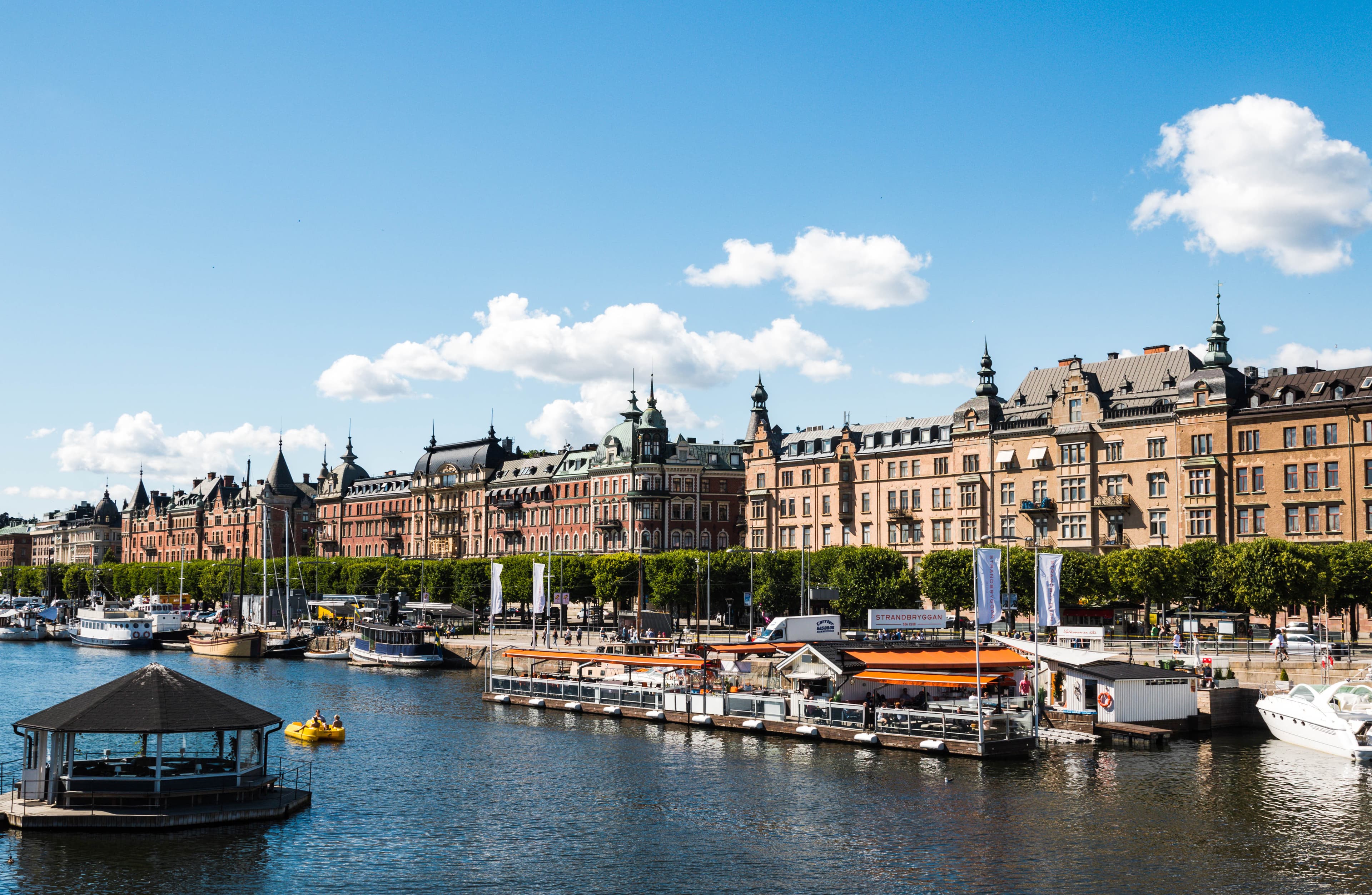 Beautiful view of townhouses along a river with boats docked to each side on a sunny day