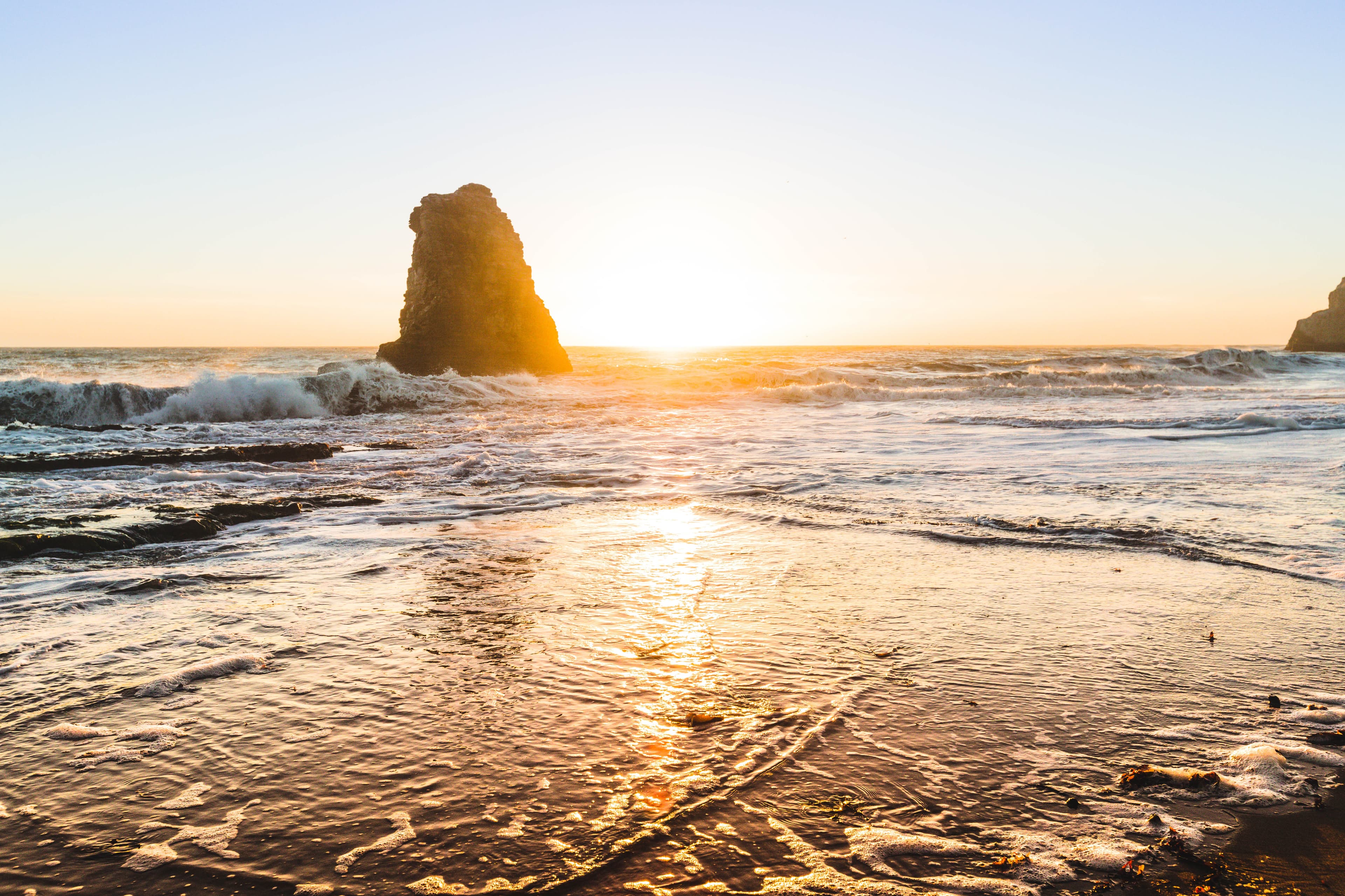 Beautiful view of the sunset over the ocean and a singular rock formation emerging from the sea