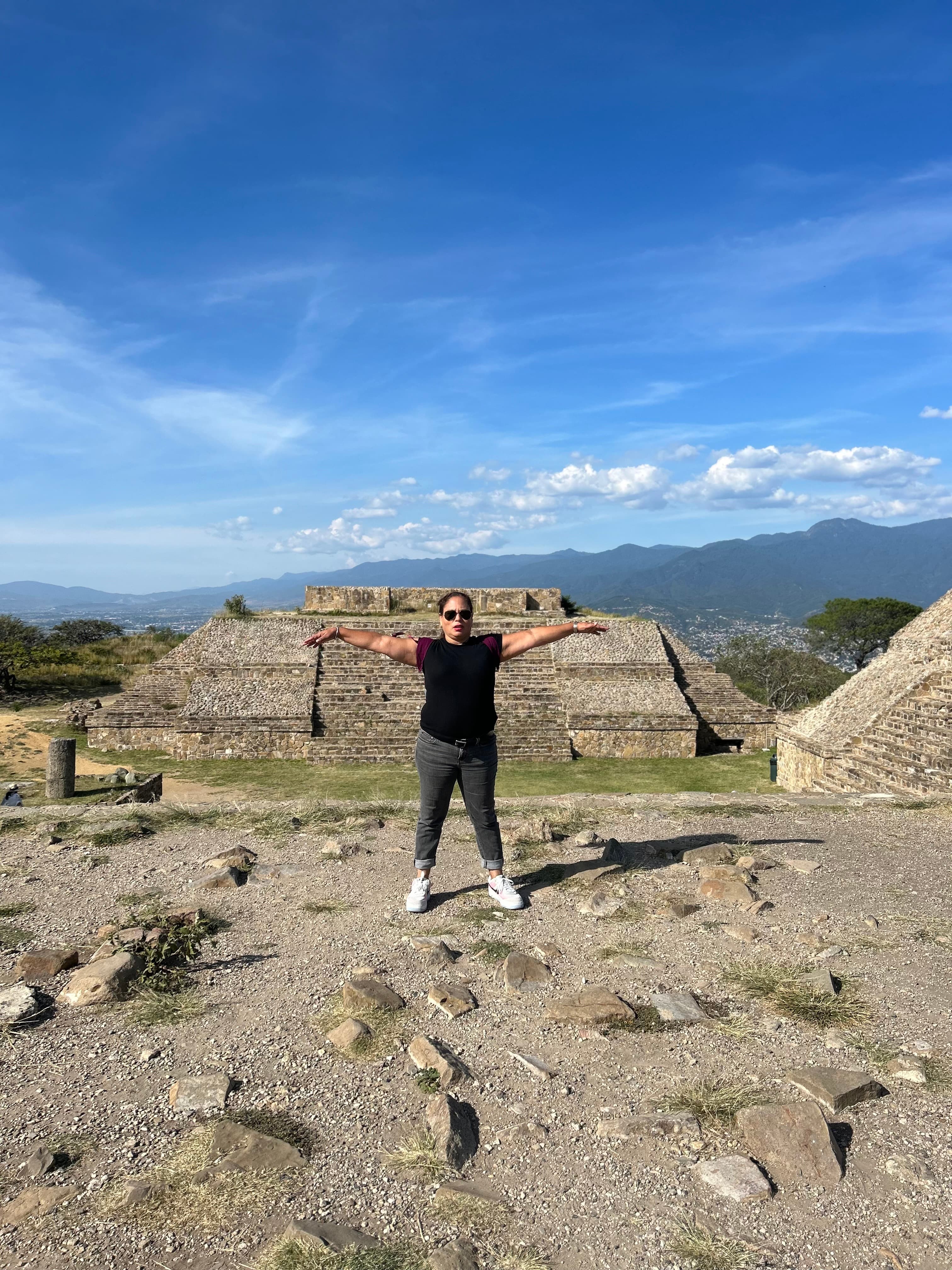 Carolina in a black t-shirt and arms outstretched in front of an ancient archaeological site on a sunny day