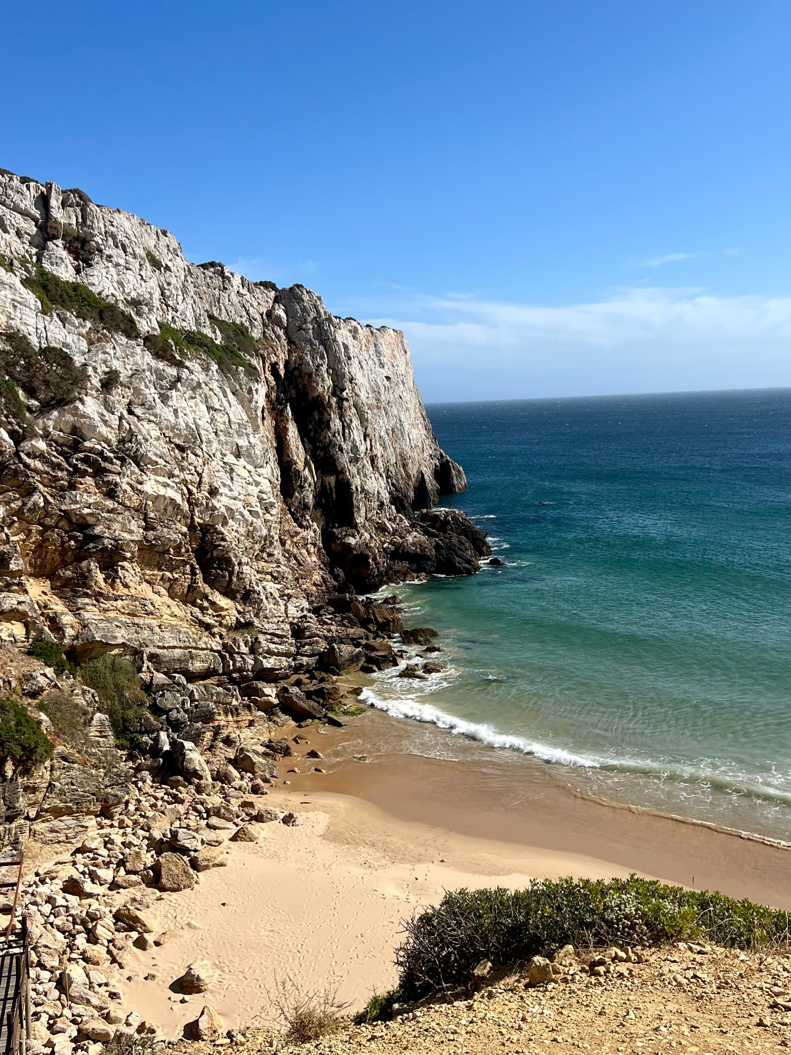 Rugged cliffs over looking the ocean and white sandy beaches on a clear day.
