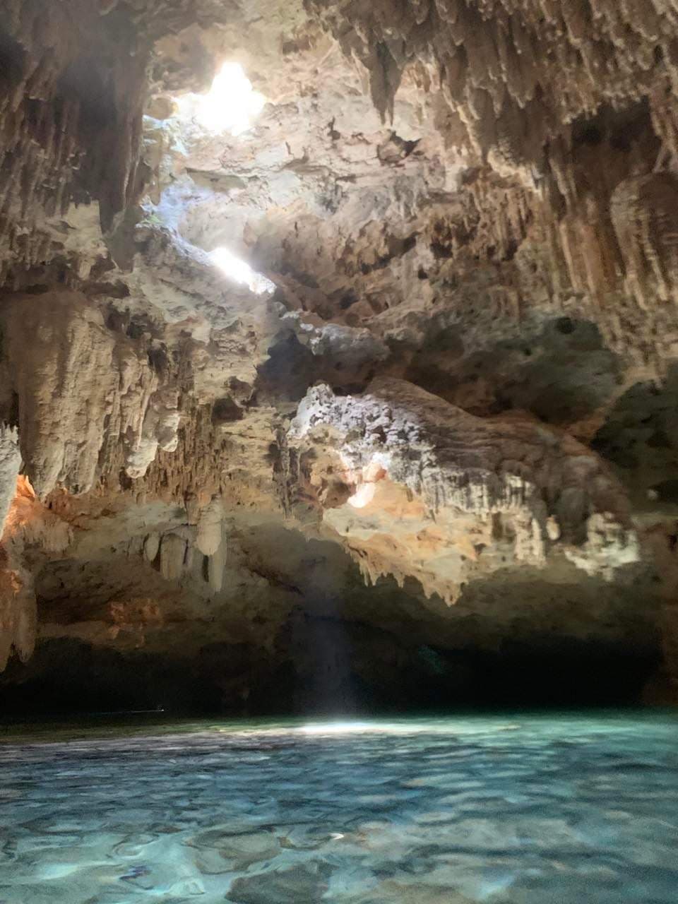 Cenote filled with blue water and light streaming through a hole in the cave ceiling.