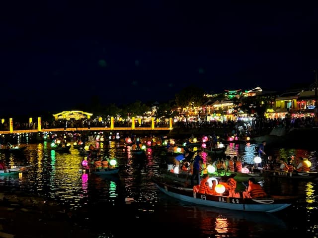 View of buildings and small boats on a river lit up with lanterns at night