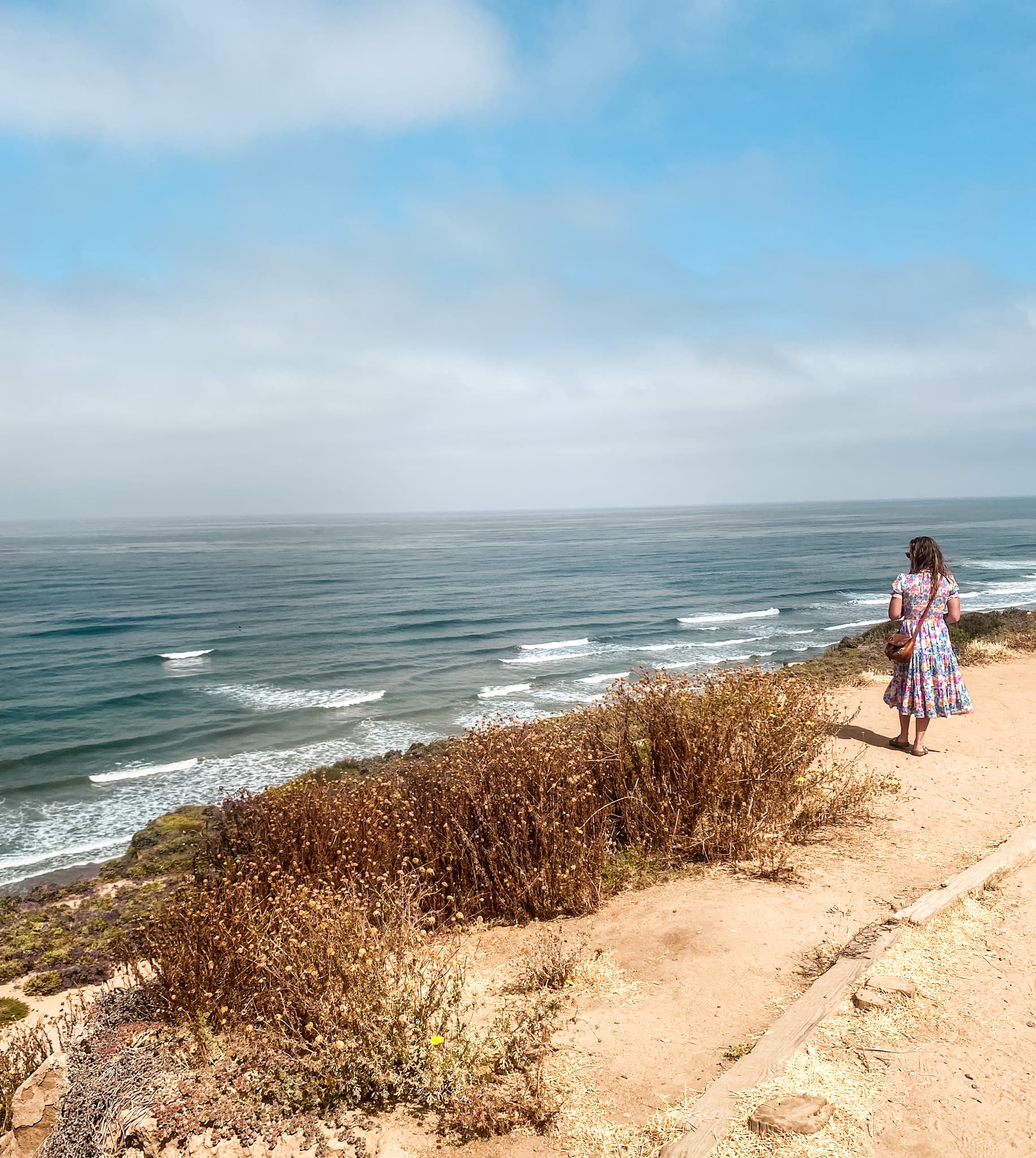 Shantel in a dress seen standing on a cliff looking out over a beautiful ocean on a sunny day