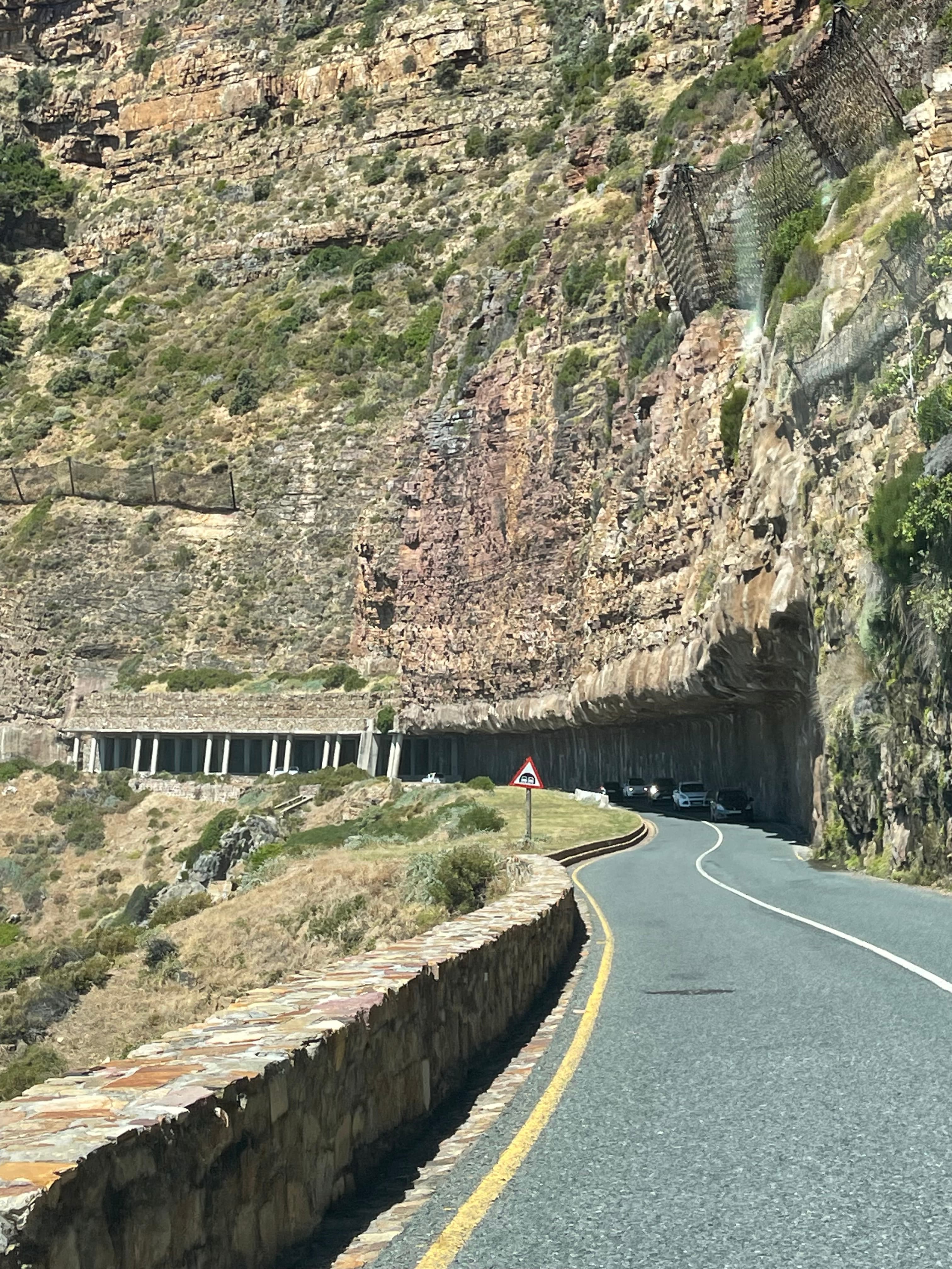 A view of a road on a hillside with a brick wall on the bluff side during the day.