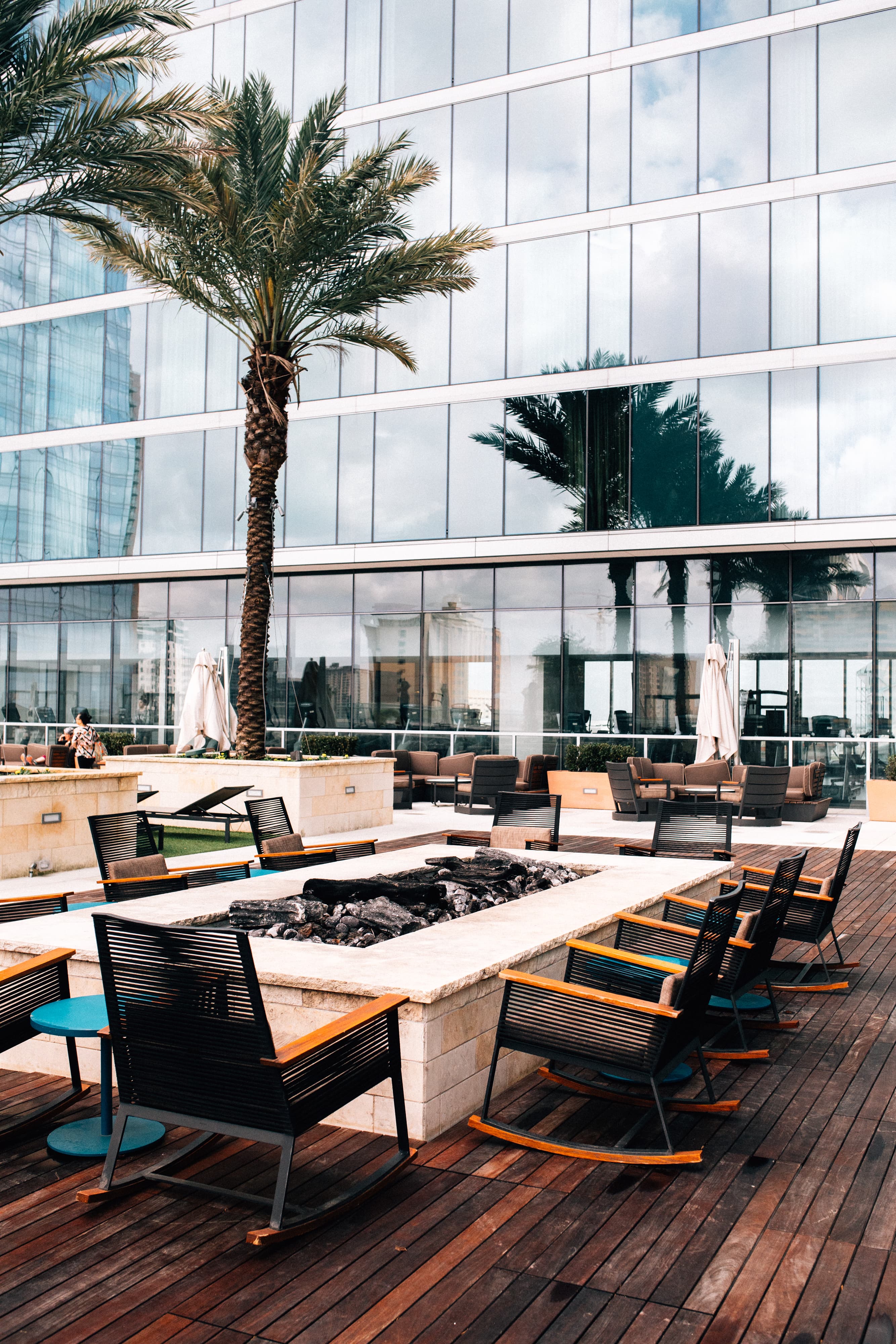 View of a fire pit surrounded by chairs and palm trees in a hotel courtyard