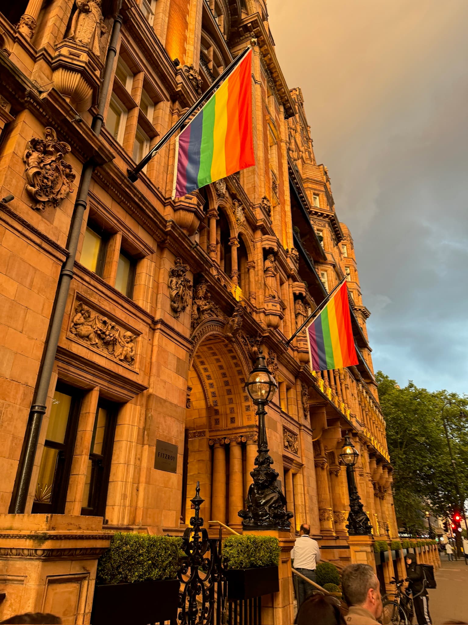 Pride flags sway off a classical building that reaches toward the sky on a cloudy day.