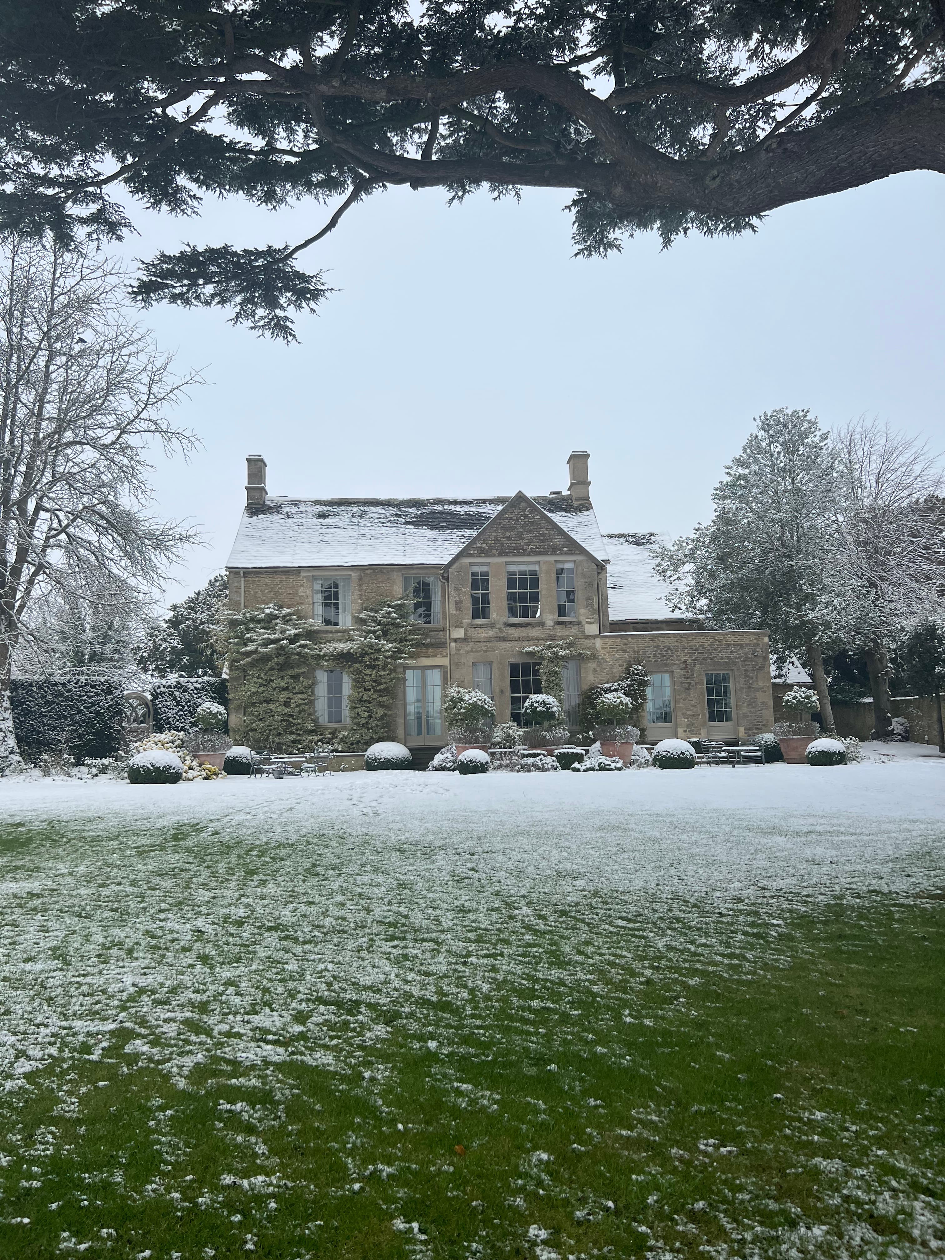 View of a pretty stone house and large yard dusted in snow